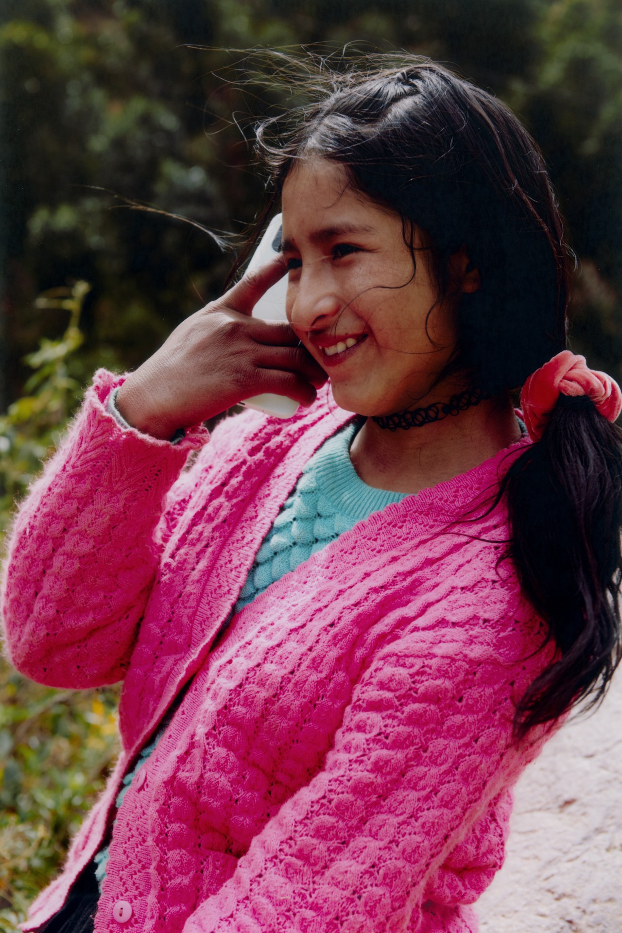 A young girl wearing a pink sweater looks away and smiles in Peru