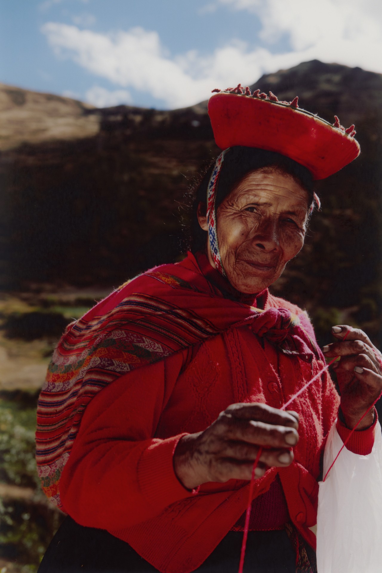 An older woman grabs onto a piece of string with the mountains behind her in Peru