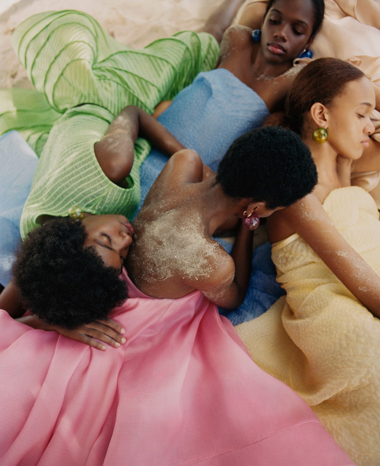A group of girls lying in sand, photographer by Nadine Ijewere. The piece is called Sisterhood in Sand