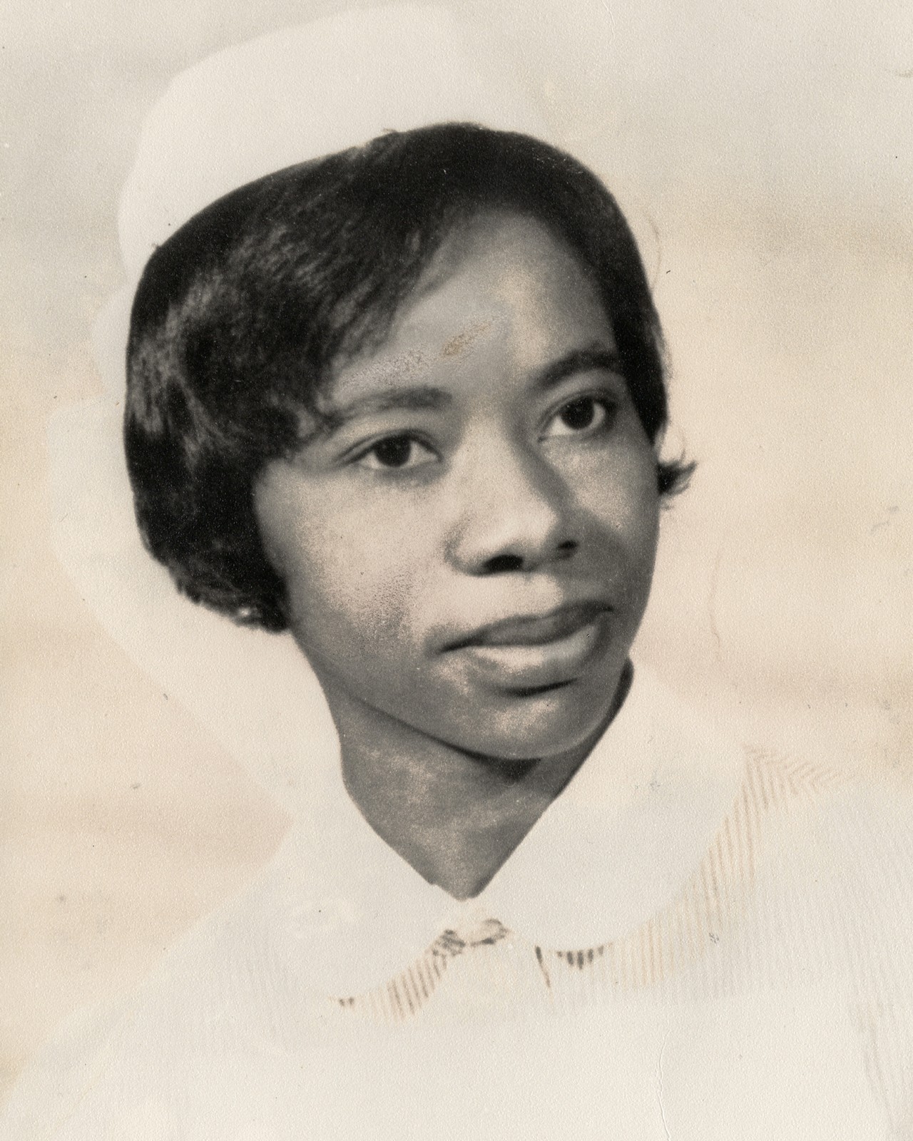 A black and white photograph of a woman wearing a white hat with a short haircut.