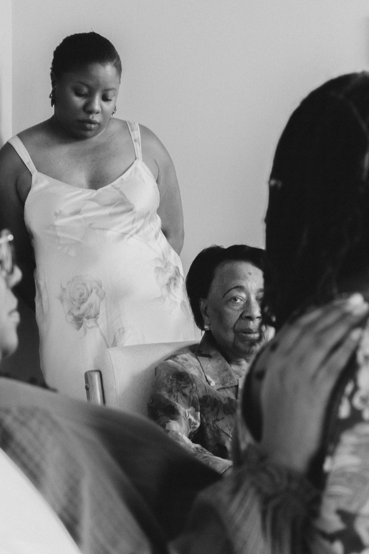 An older woman sits as a younger woman wearing a dress stands behind her.