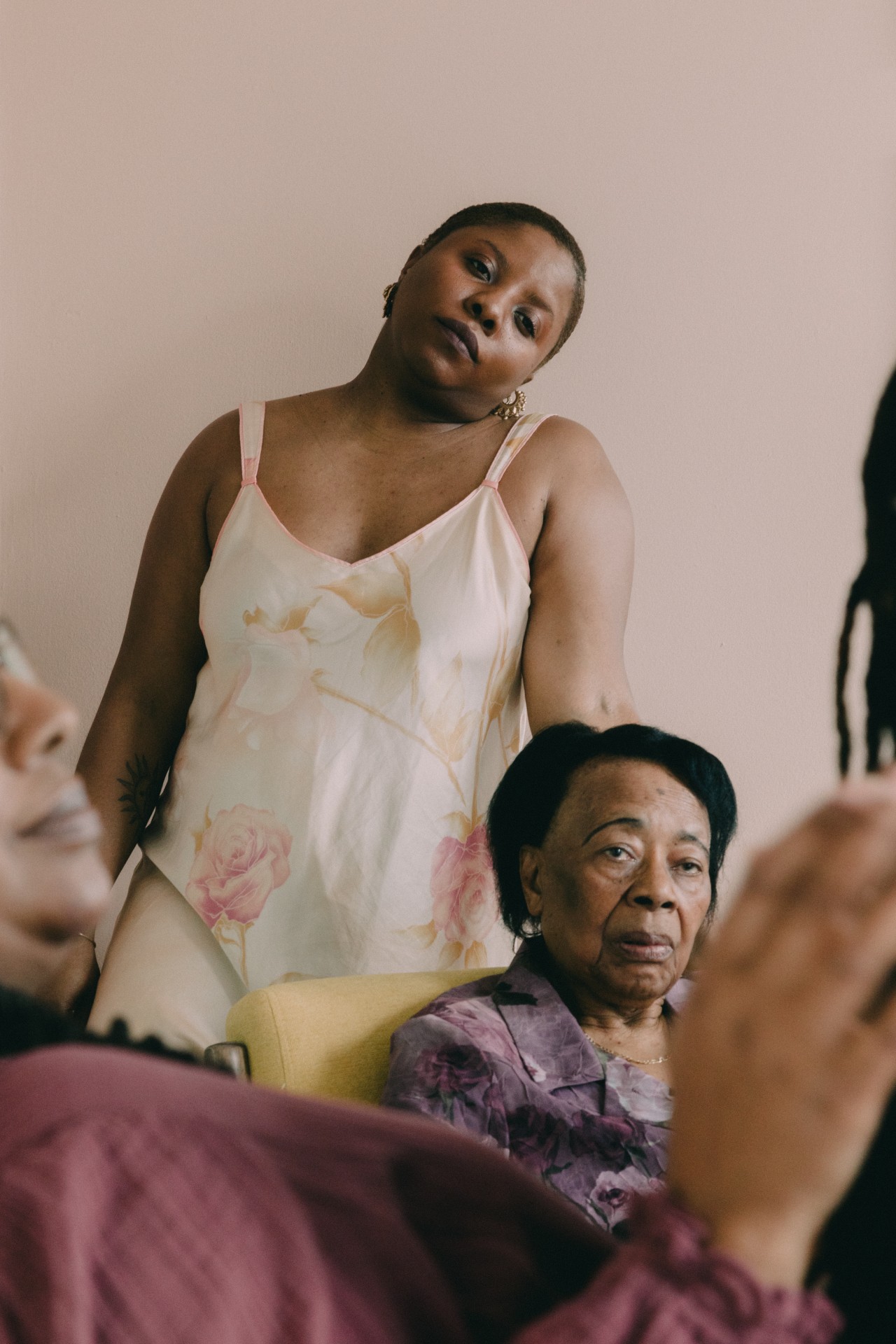 A younger woman stands behind an older woman sitting in a chair inside of a home.