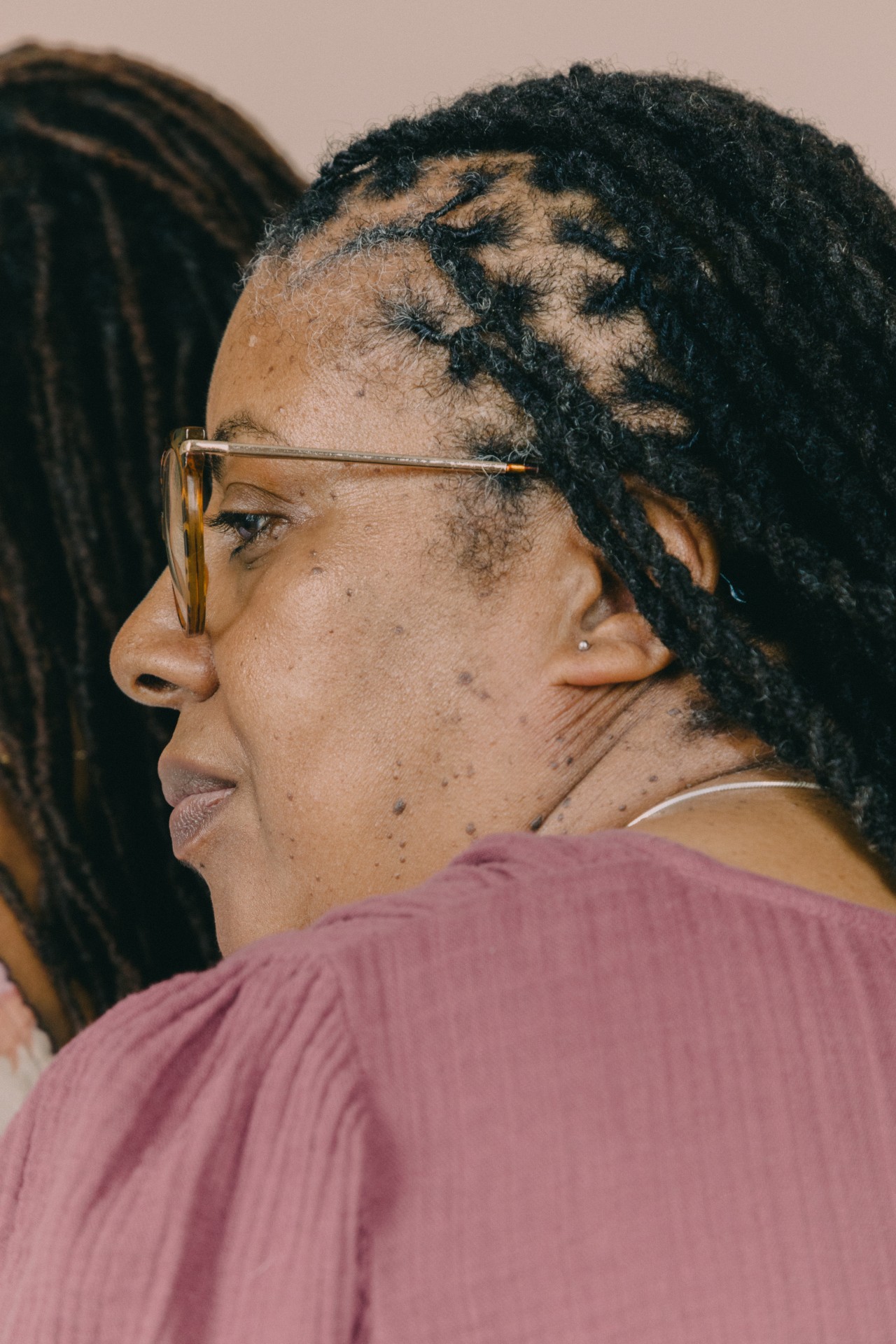 The profile of an older woman with glasses and locs.