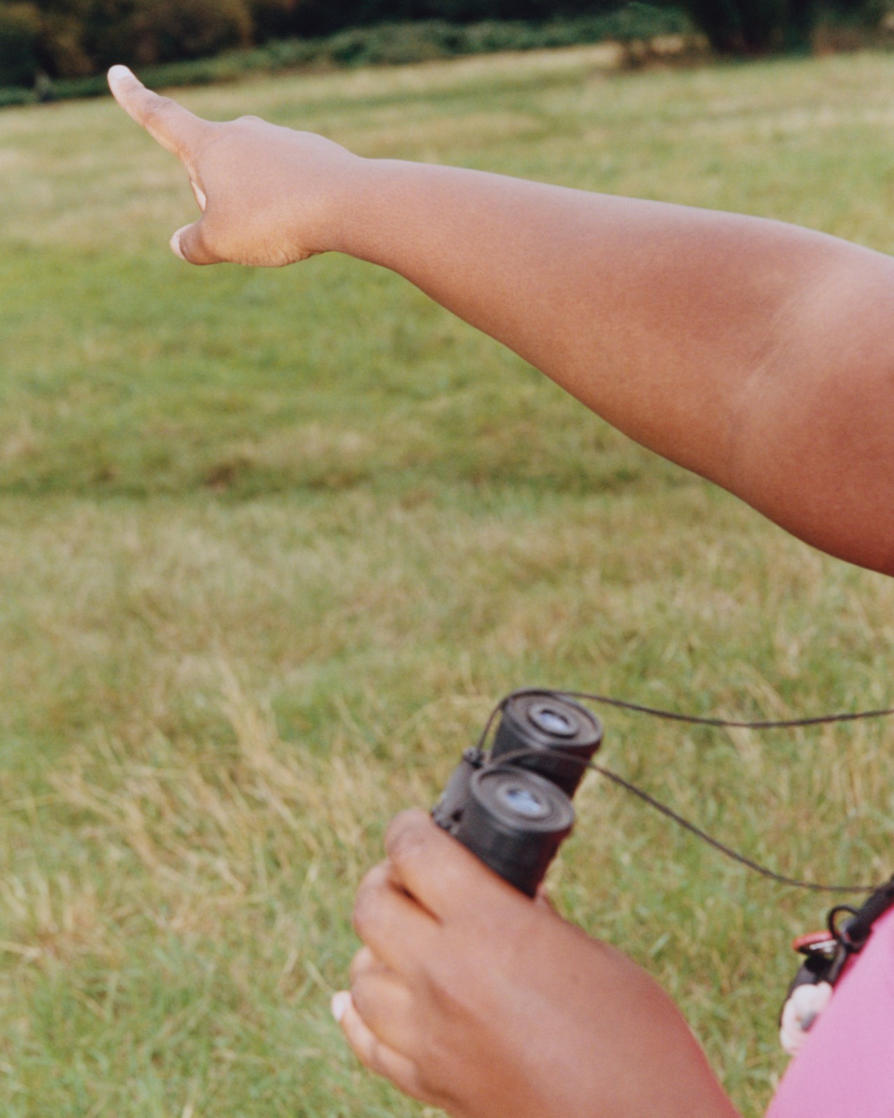 A person point up with their finger while holding binoculars in their other hand.