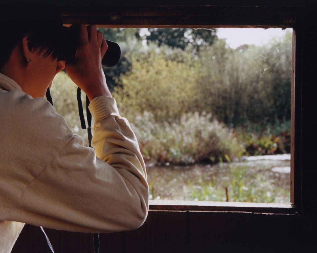 A person looks out a window with binoculars