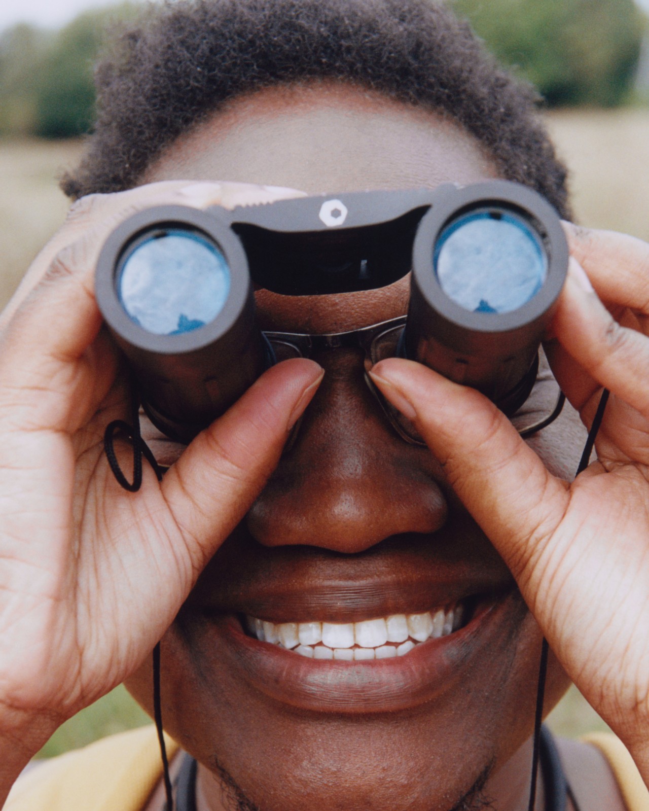 A close up of a person smiling and looking through binoculars.