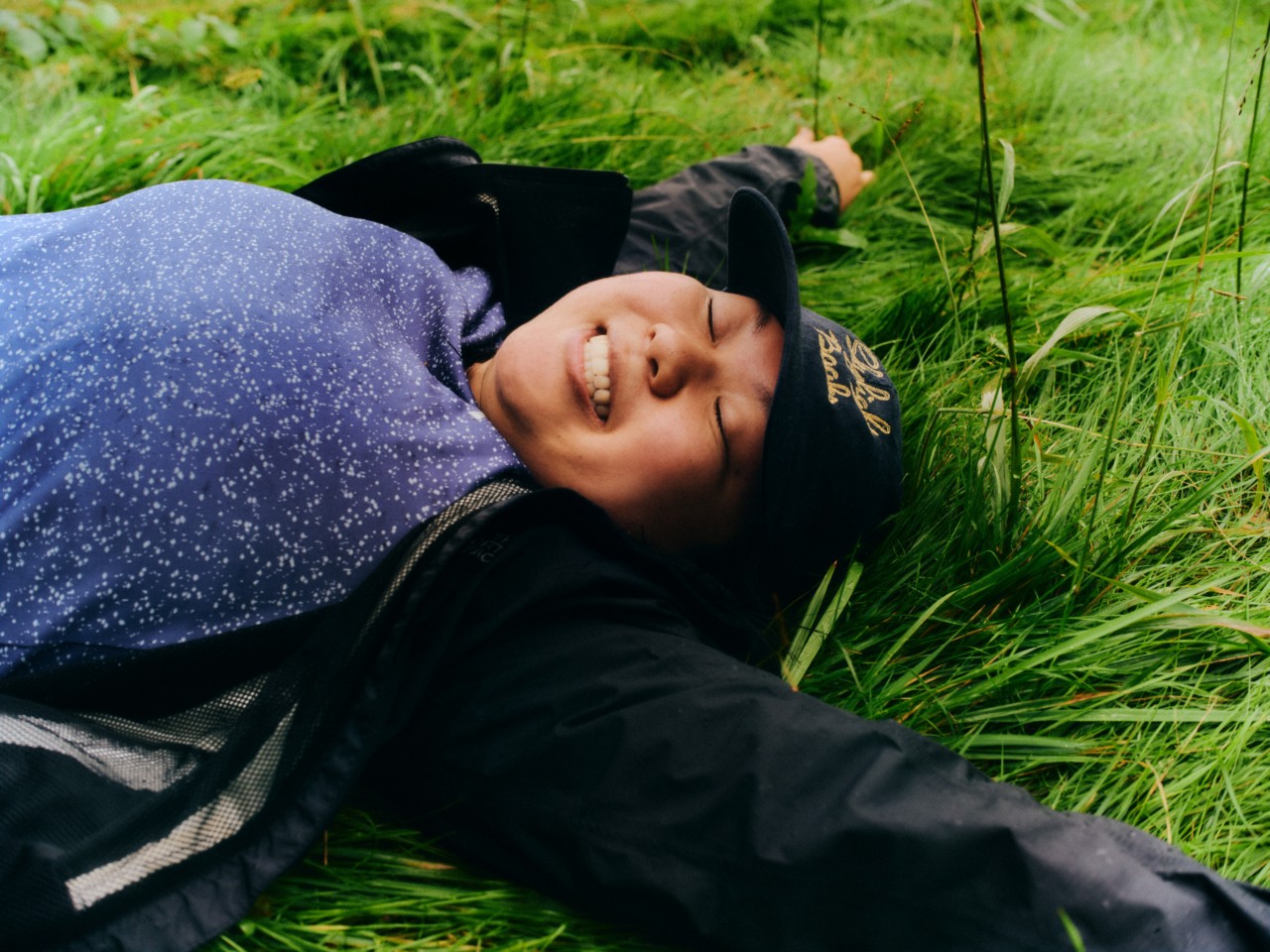 A person smiles while laying down in the grass.