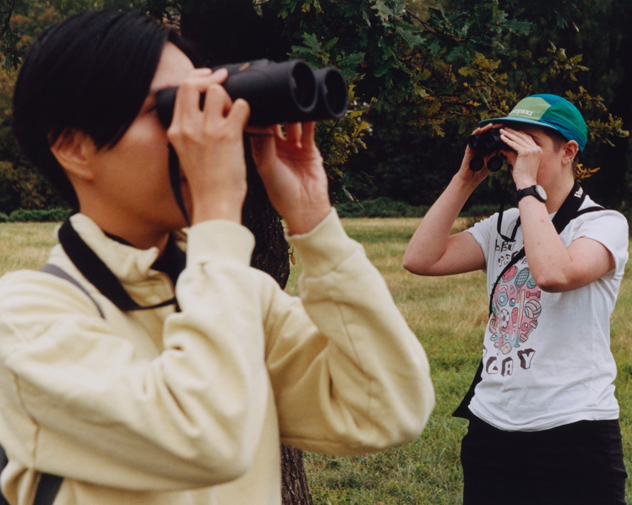 Two people look in opposite directions with their binoculars.