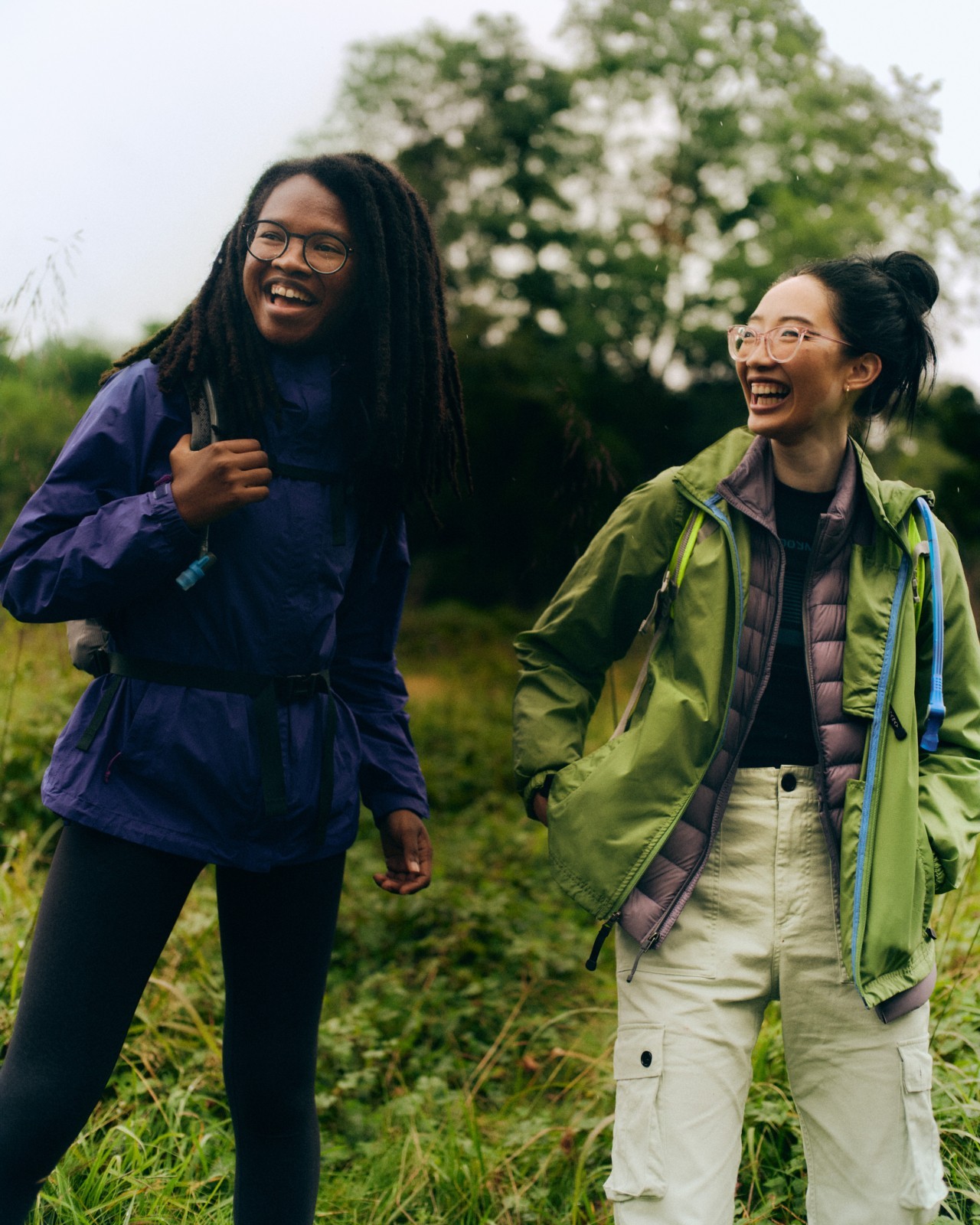 Two people laugh while standing in a grassy forest.