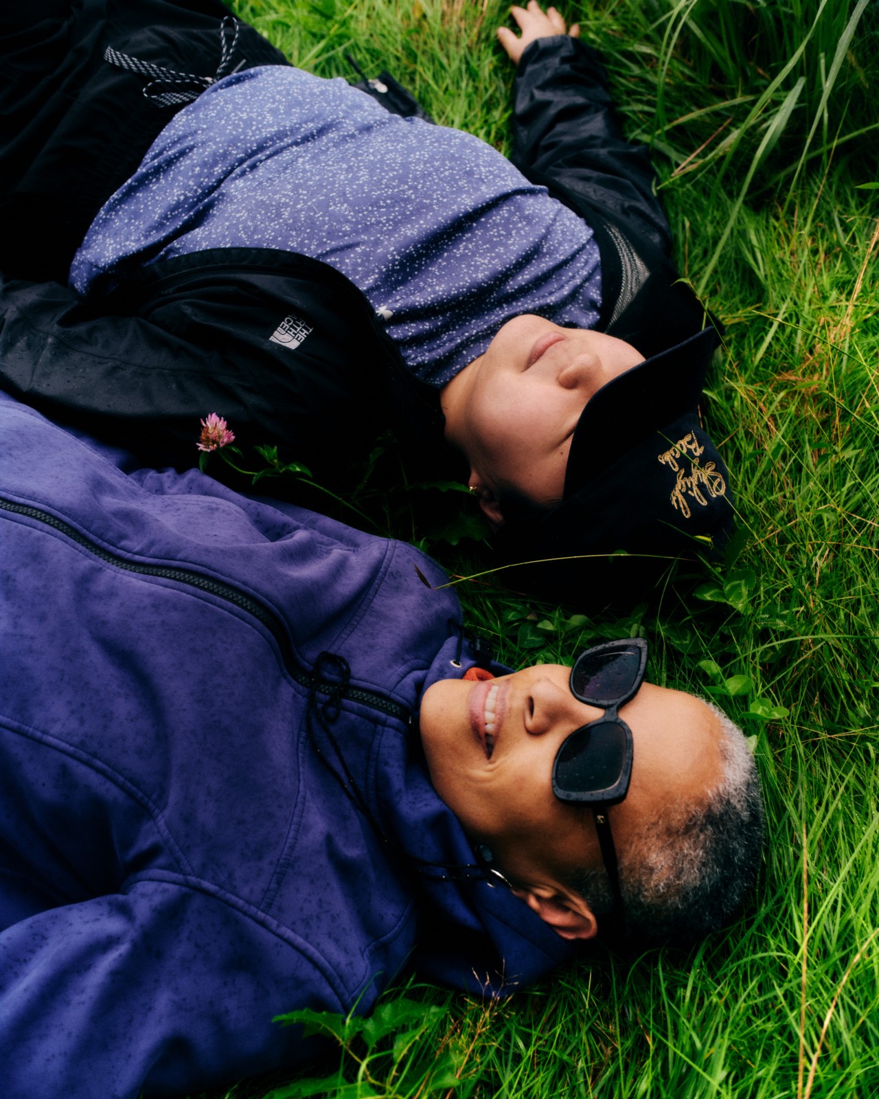 Two people lie down next to each other in the grass