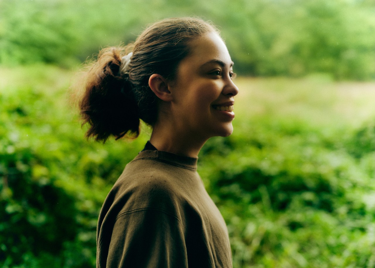 The profile of a person with a curly ponytail, standing amidst greenery