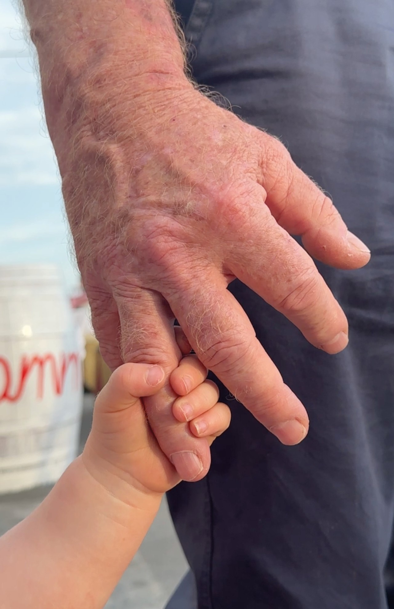 A small baby hand holds onto the ring finger of a large adult hand.