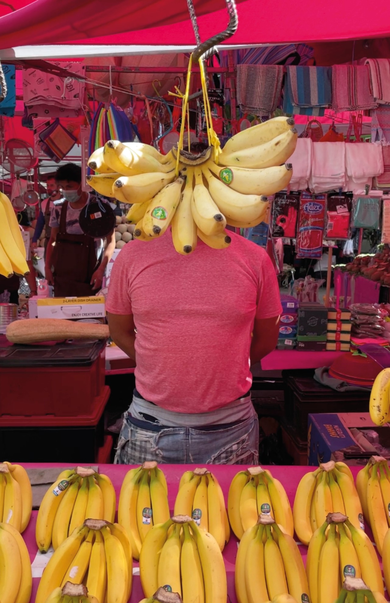 A bunch of bananas hang in front of a person standing at a bandana stand.