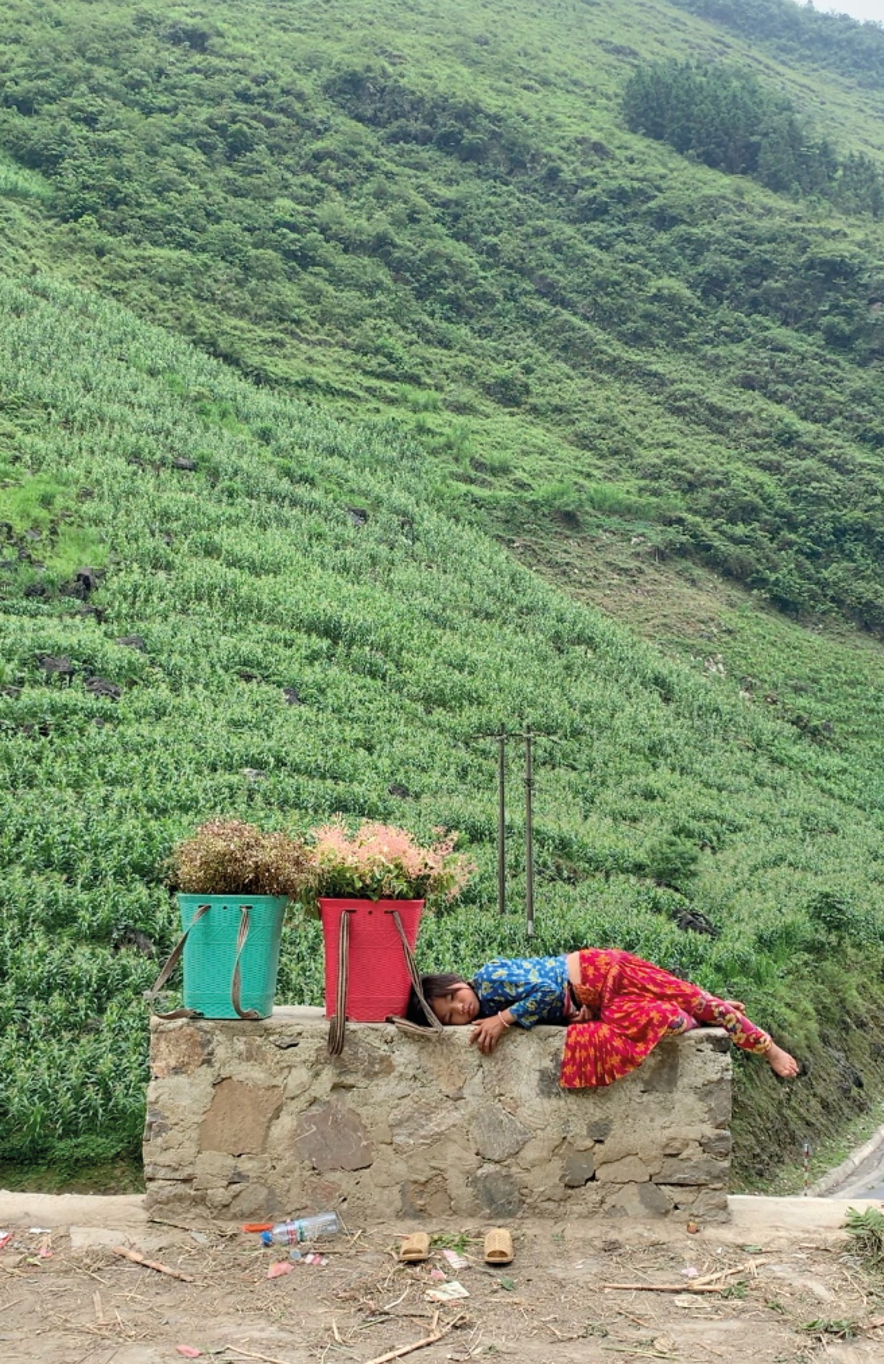 A child lays down on a concrete block in front of a grassy mountain.