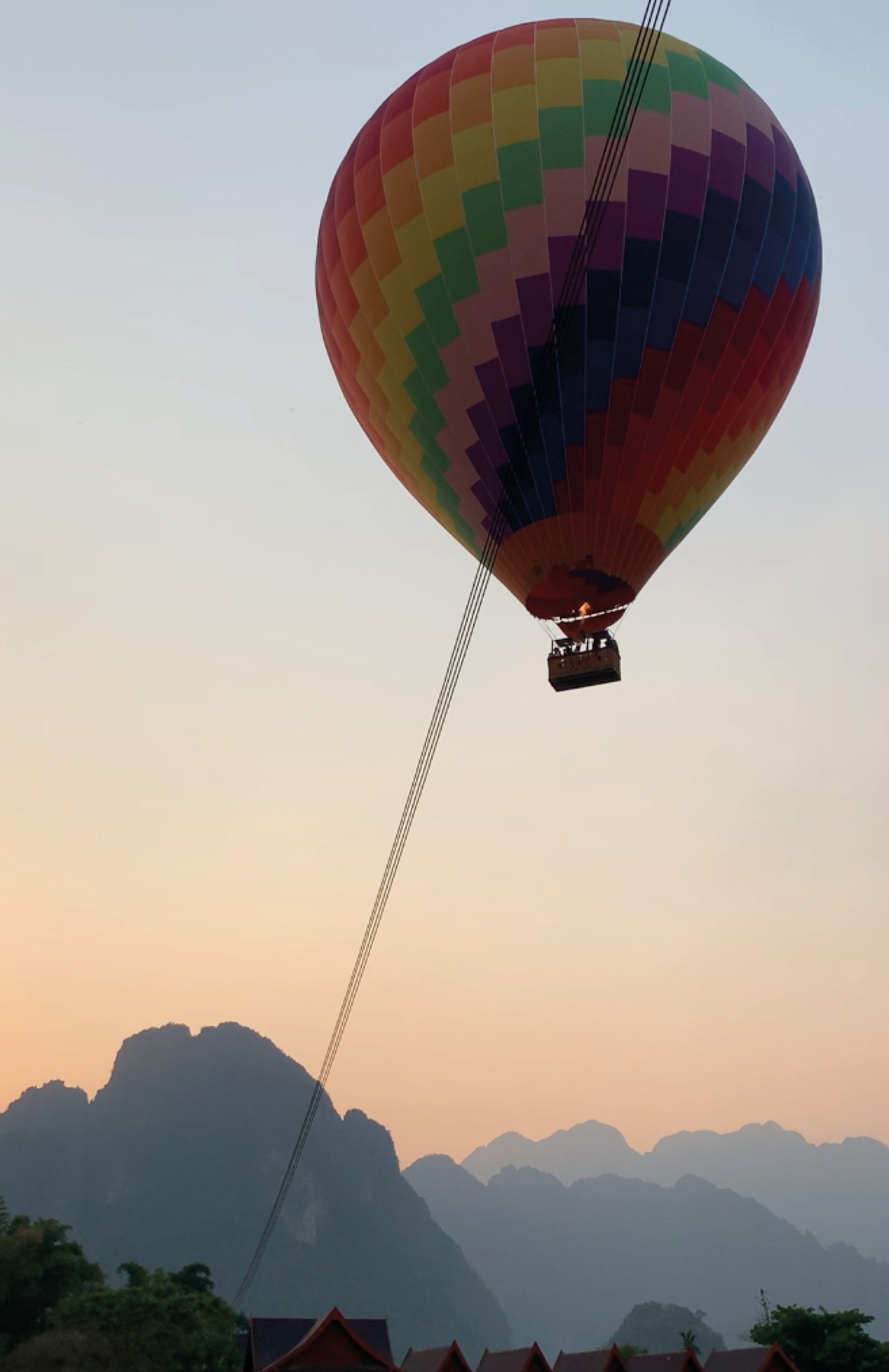 A rainbow hot air balloon flies high above the mountains during sunset.