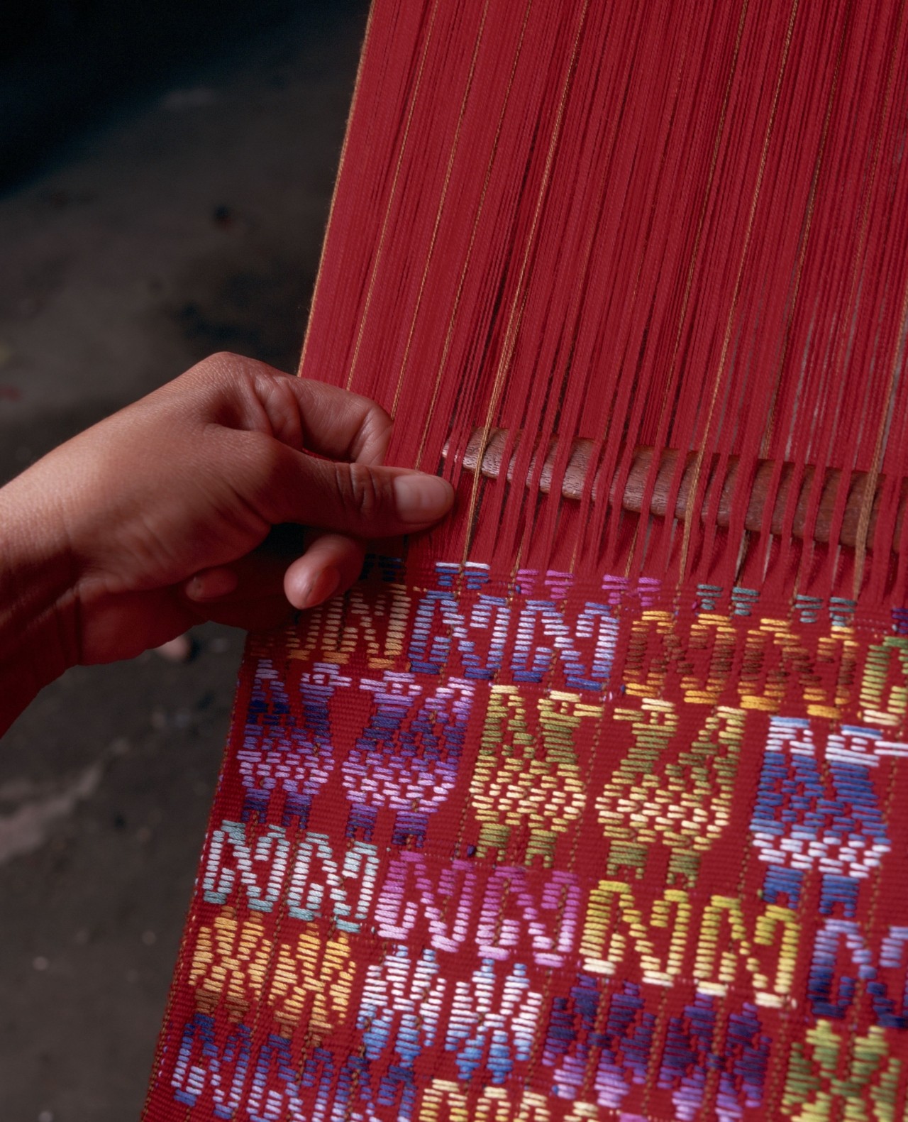 A hand caresses a red, indigenous piece of clothing