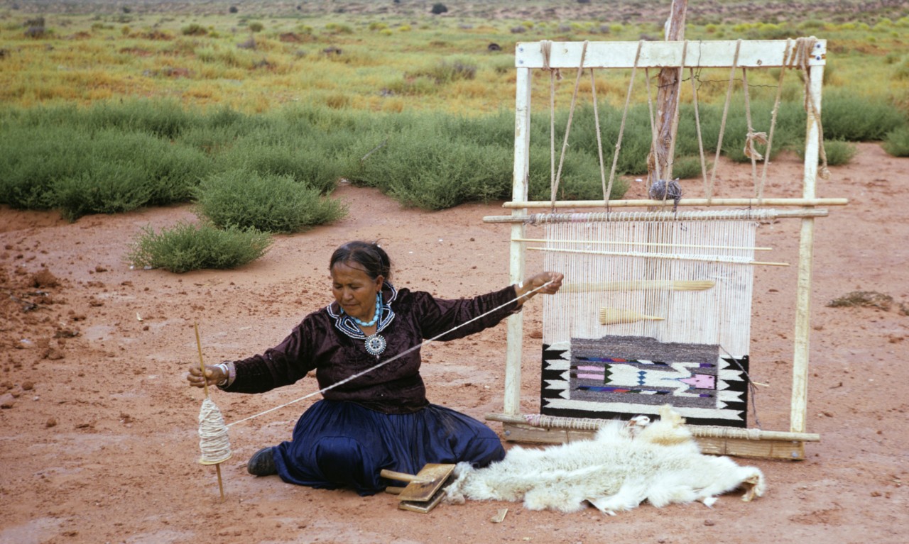An indigenous woman sits on the ground while making indigenous clothes.
