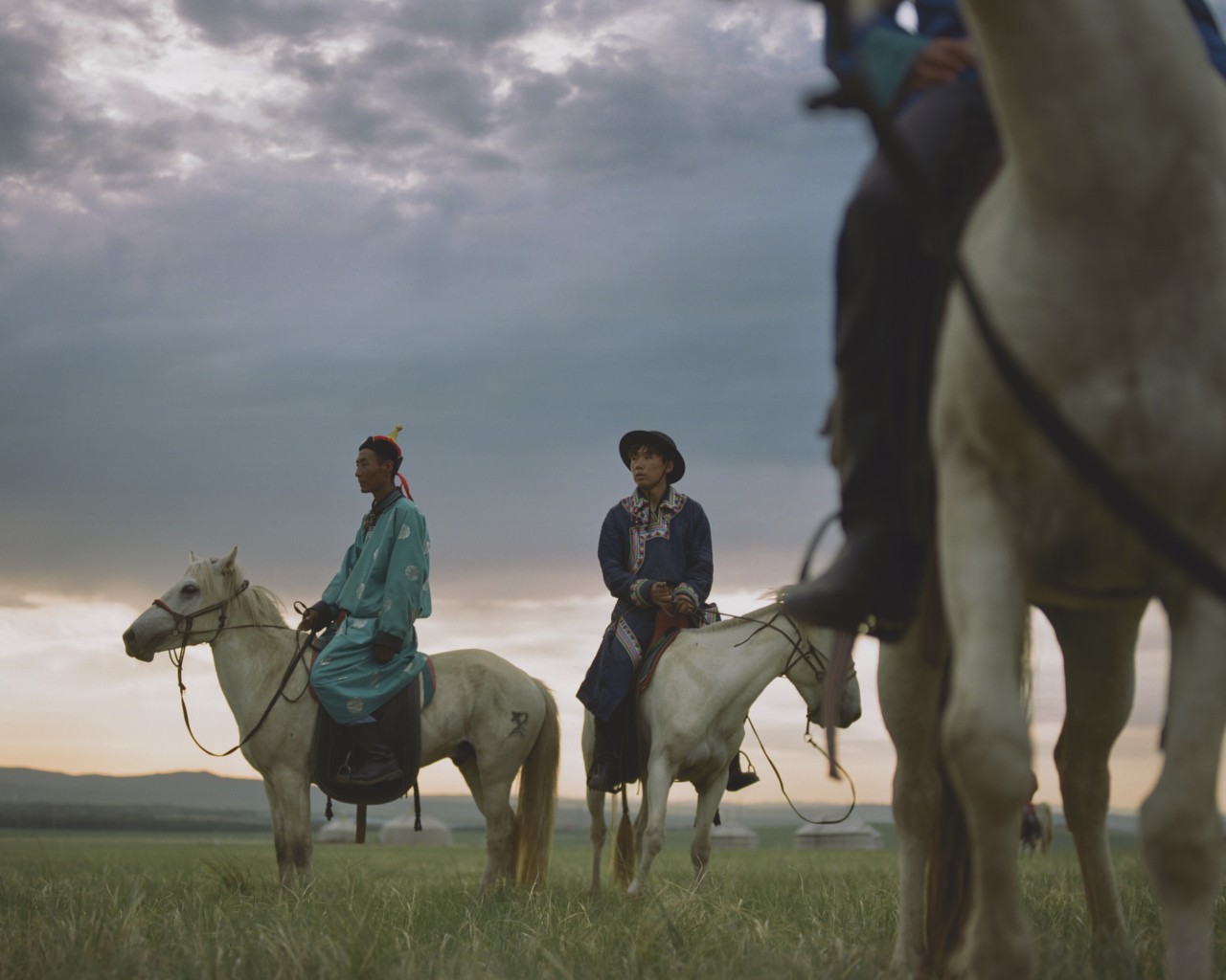 A small group of Mongolian people sit on top of their horse in an open field.