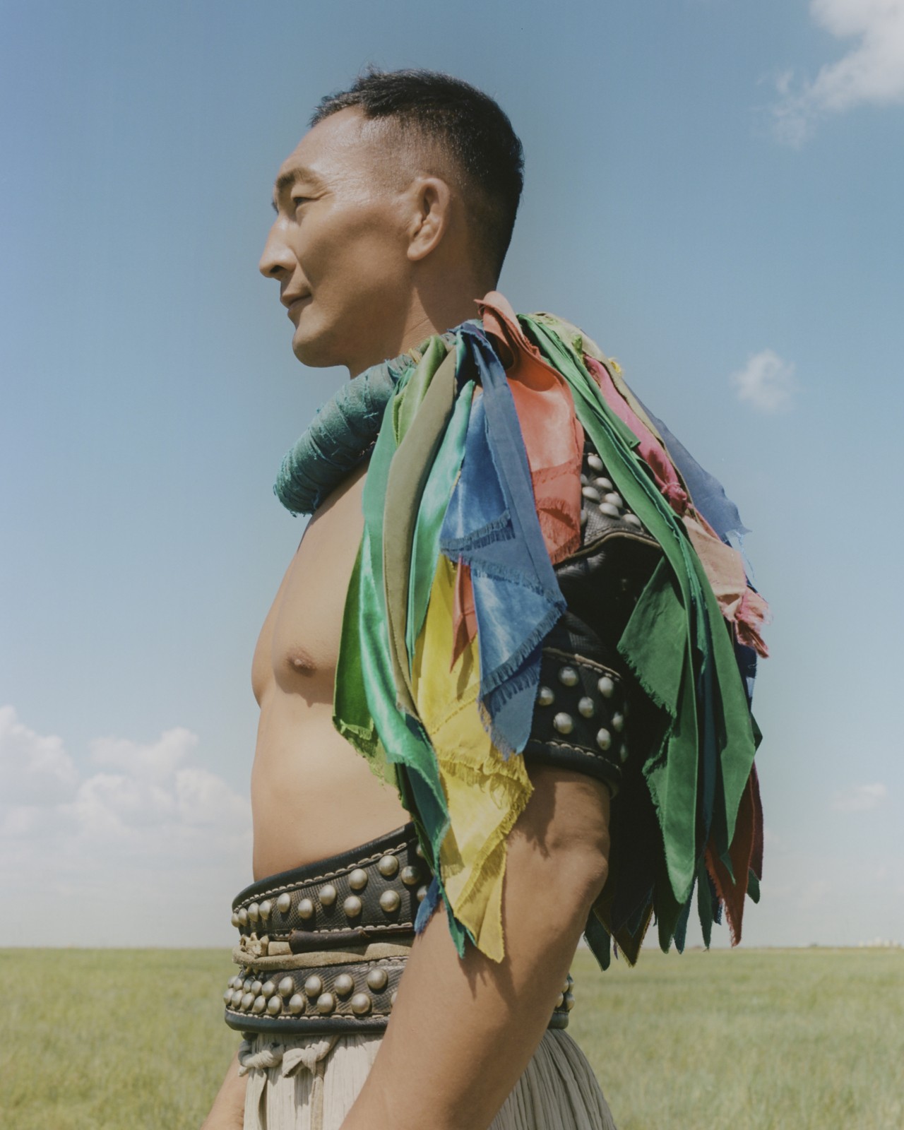 The profile of a Mongolian person standing in a field, wearing a colorful cape.