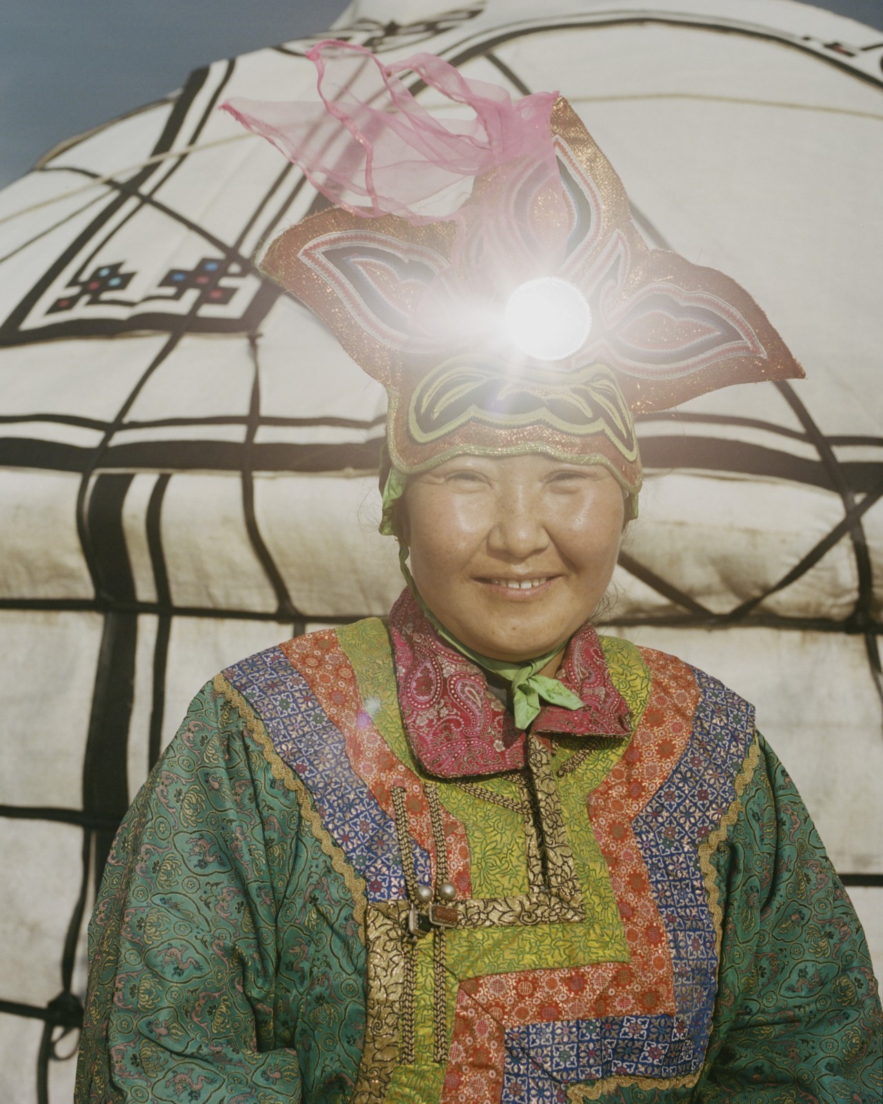 A Mongolian person dressed in traditional garb smiles at the camera.
