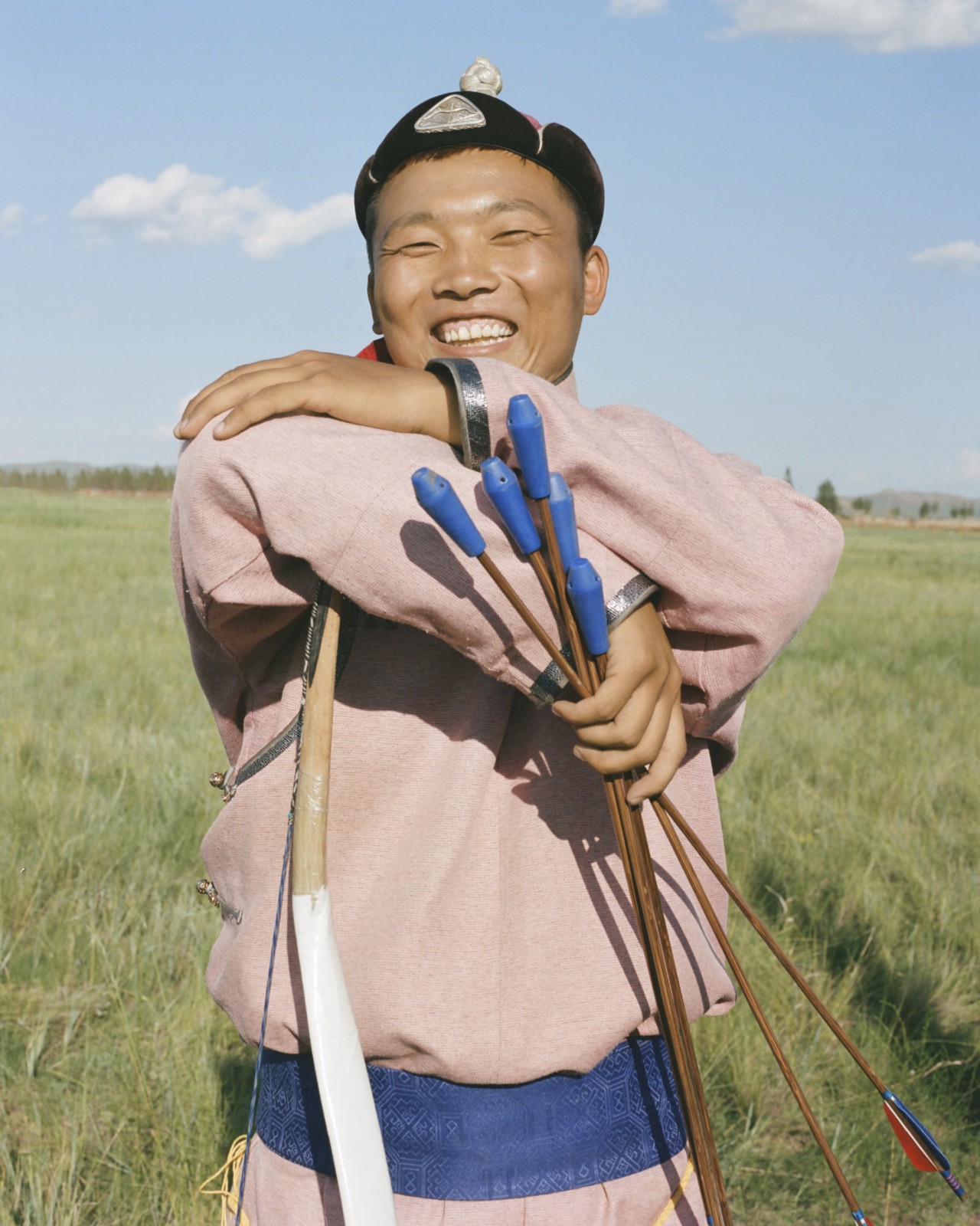A Mongolian person smiles while holding a bunch of arrows in their hand.