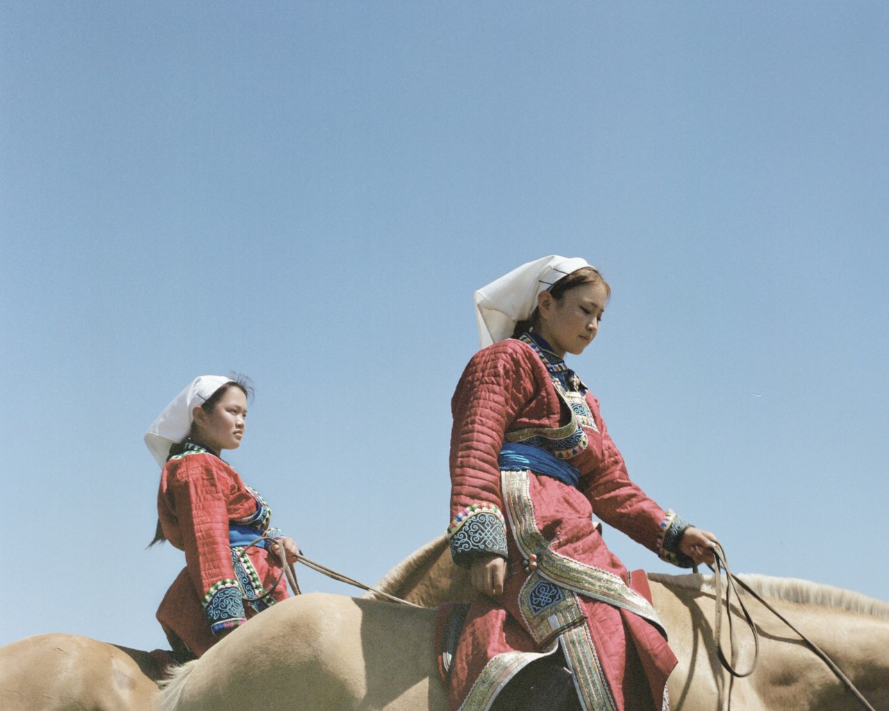 Two Mongolian women dressed the same ride horses.