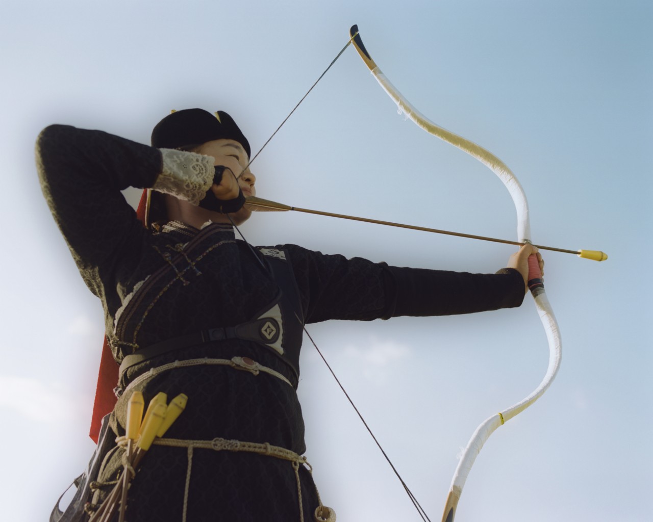A Mongolian person shoots a bow and arrow.