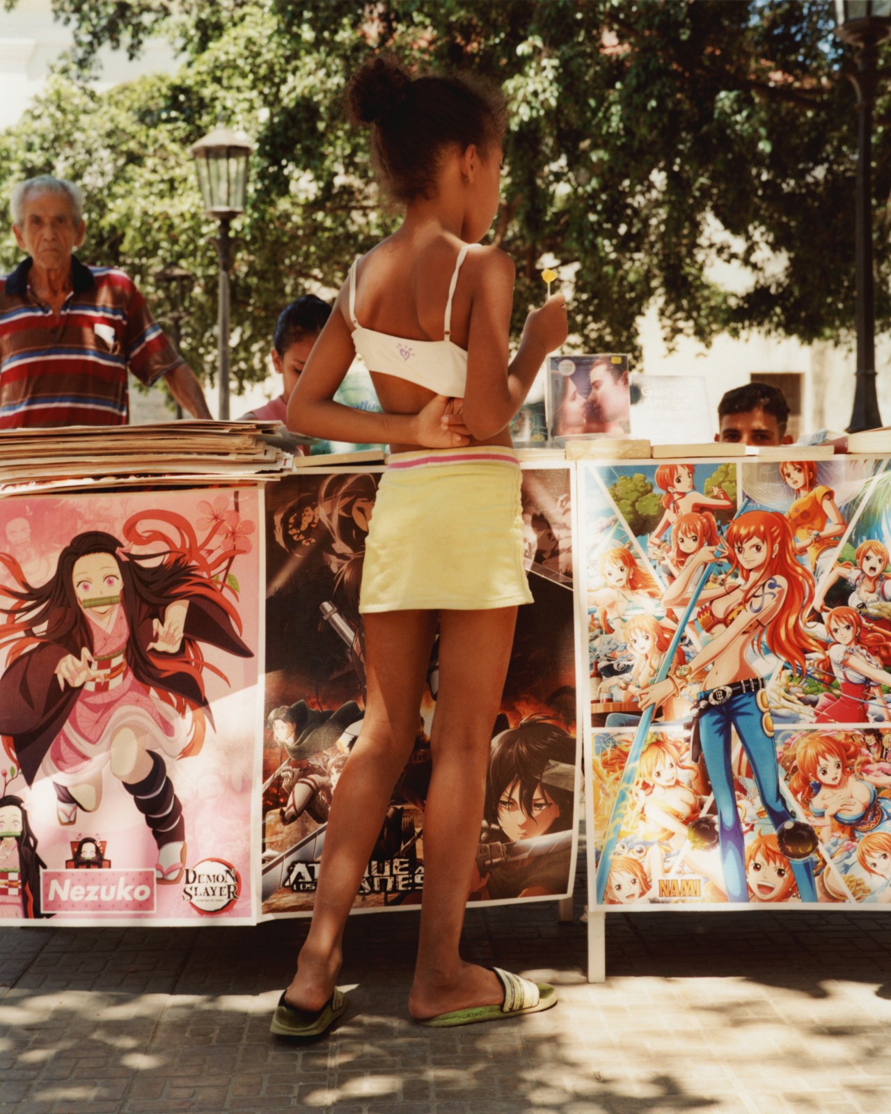 A child dressed in a yellow skirt and white tank stands facing away from the camera.