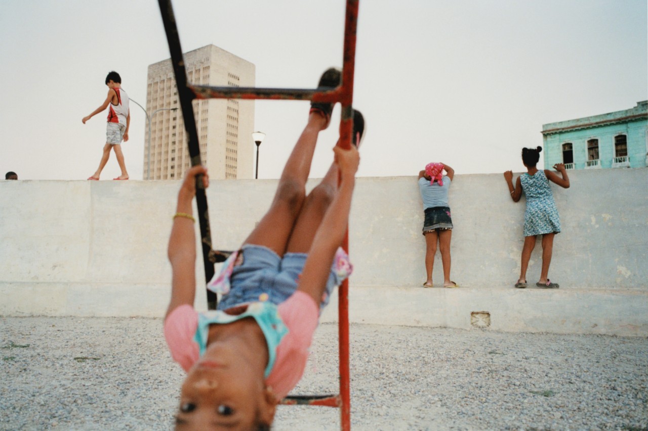 A young child hangs upside down on a ladder swing.