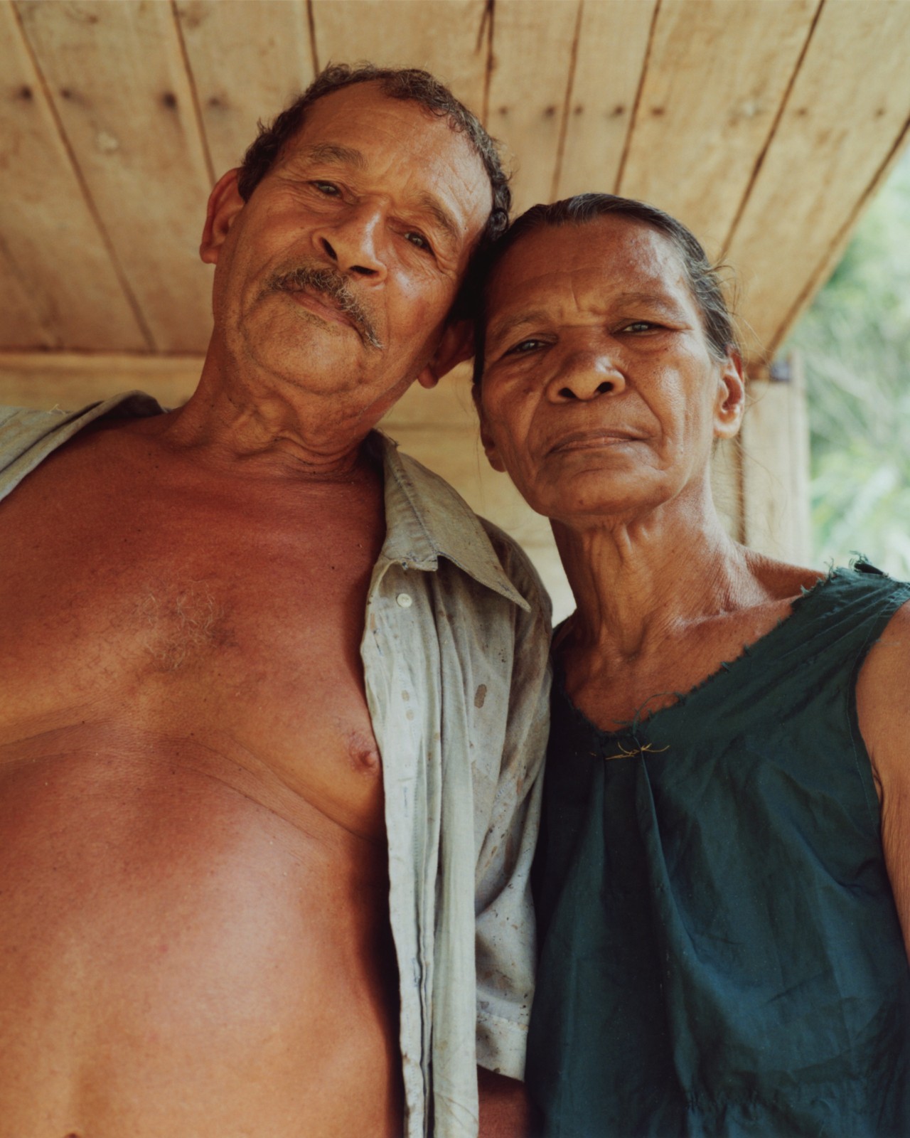 Two older people rest their heads on one another as they peer into the camera.