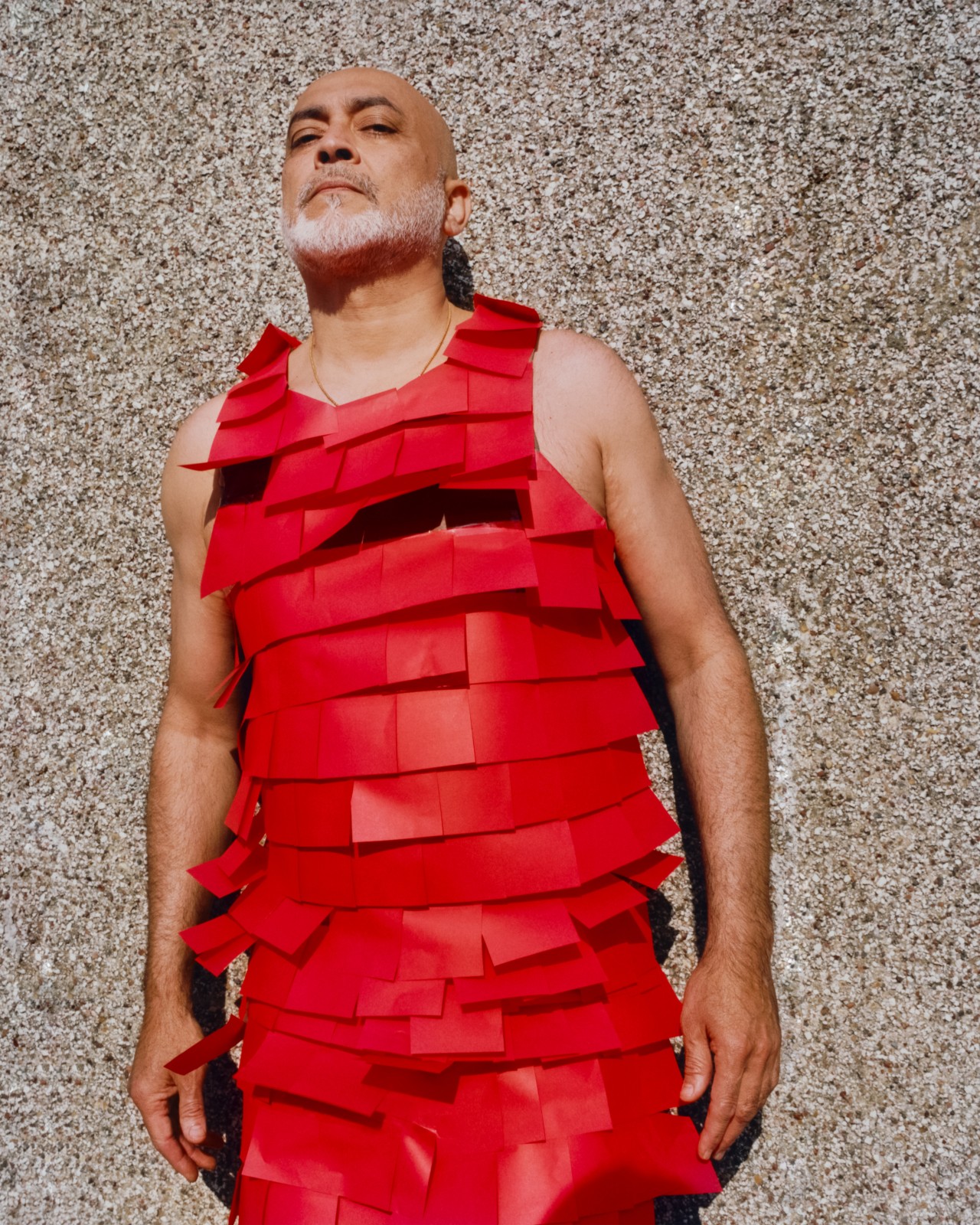 Someone poses in front of a concrete wall while wearing a dress made of red post it notes.