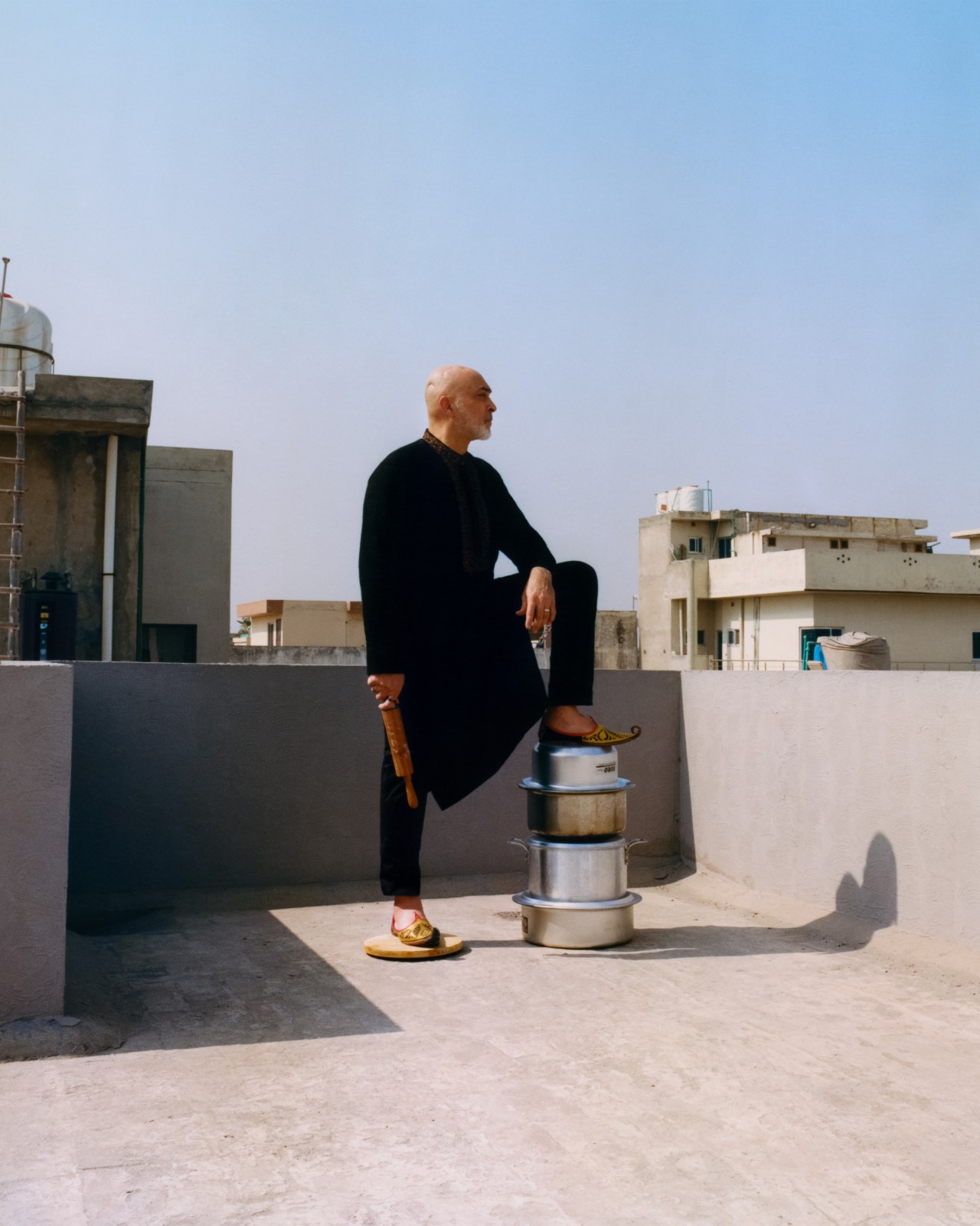 A person on the roof of a building rests their leg on top a stack of pots.