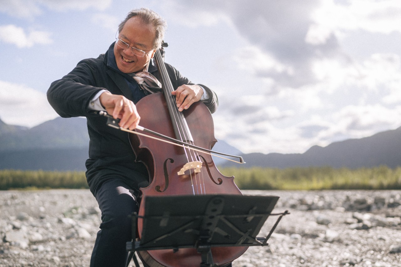 Yo Yo Ma plays the cello on a mountainous landscape.