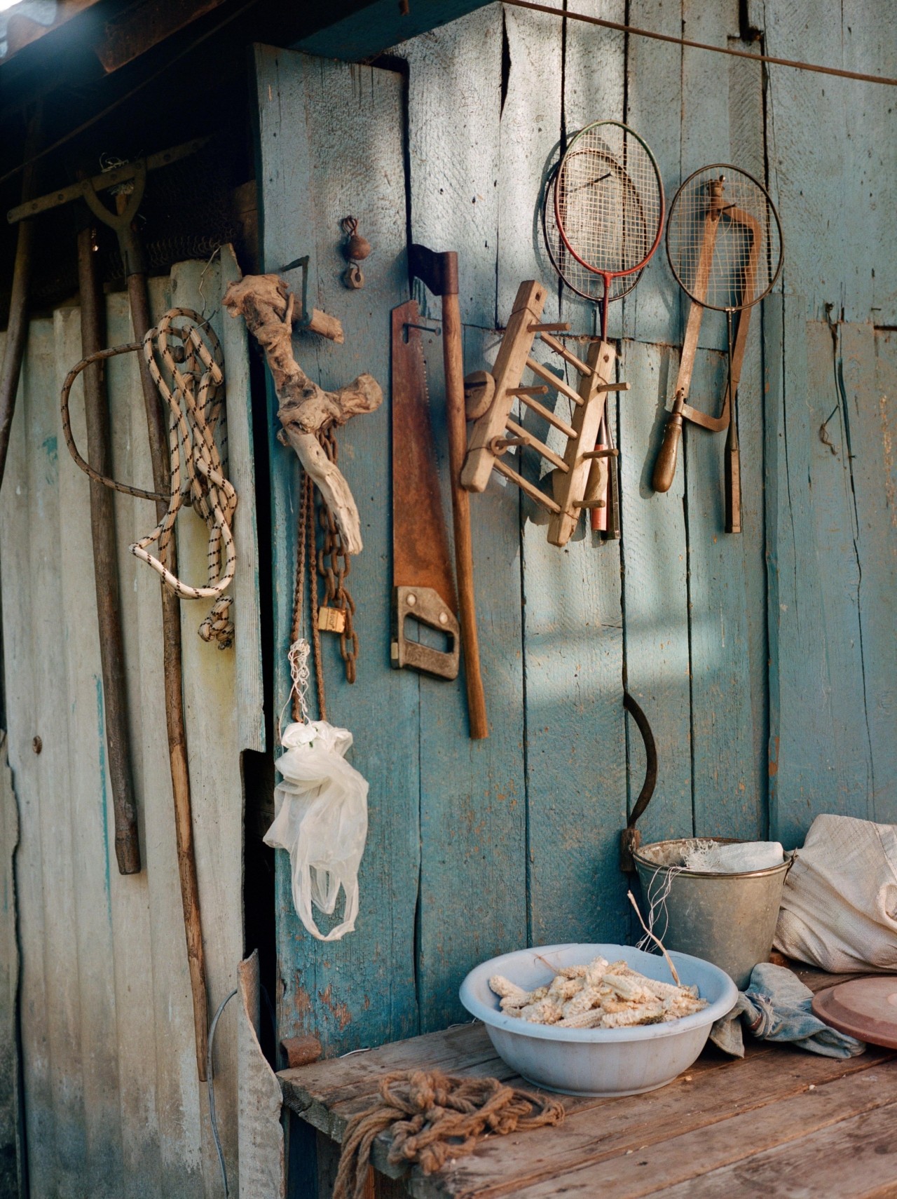 Several tools hang on the side of a blue shed.