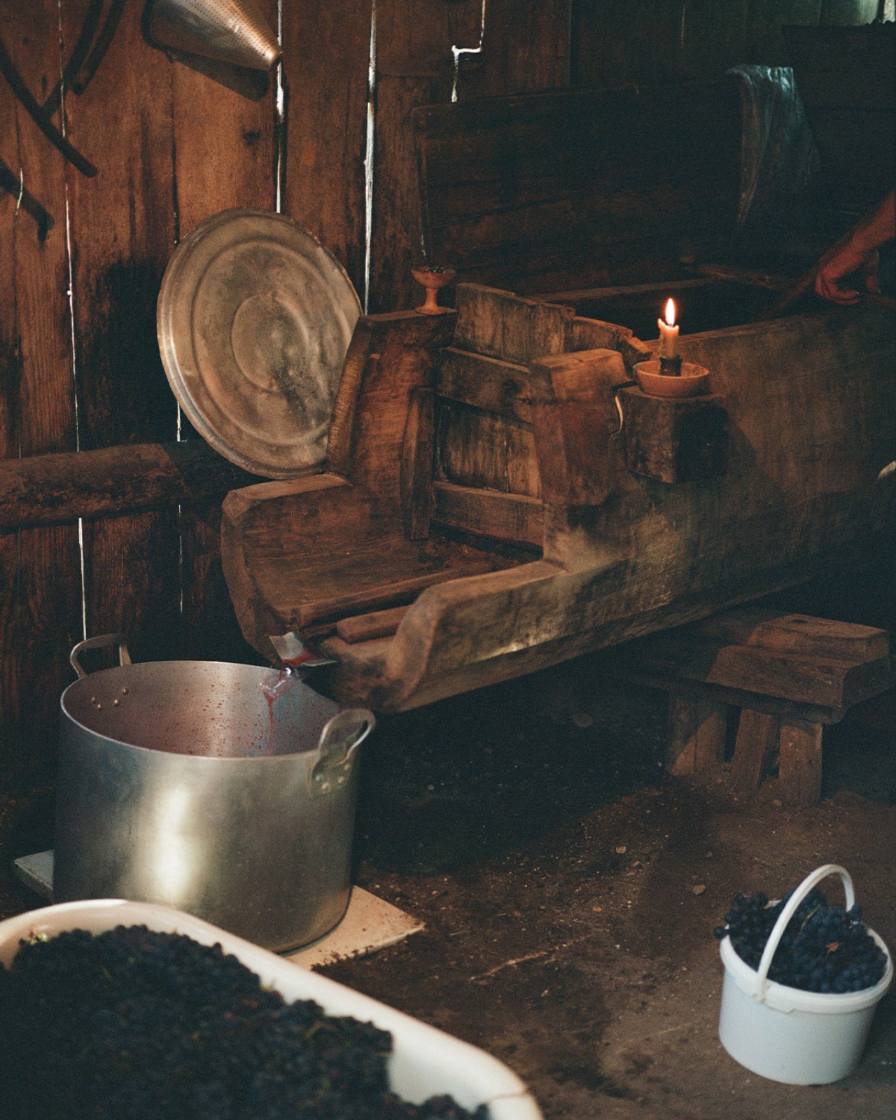 A candle burns in a dark, crowded wooden shed.