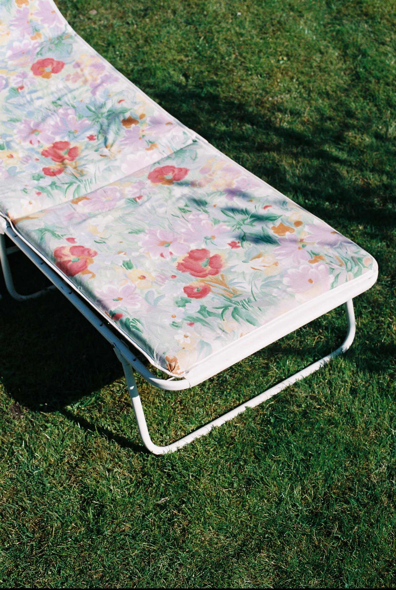 A lawn chair with a colorful flower patterns lies still in a grass field.