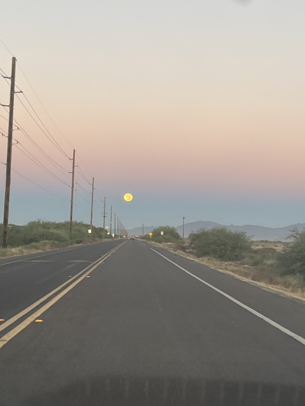 The moon. shines in the distance of a hazy pink sky. An empty road leads to nowhere.