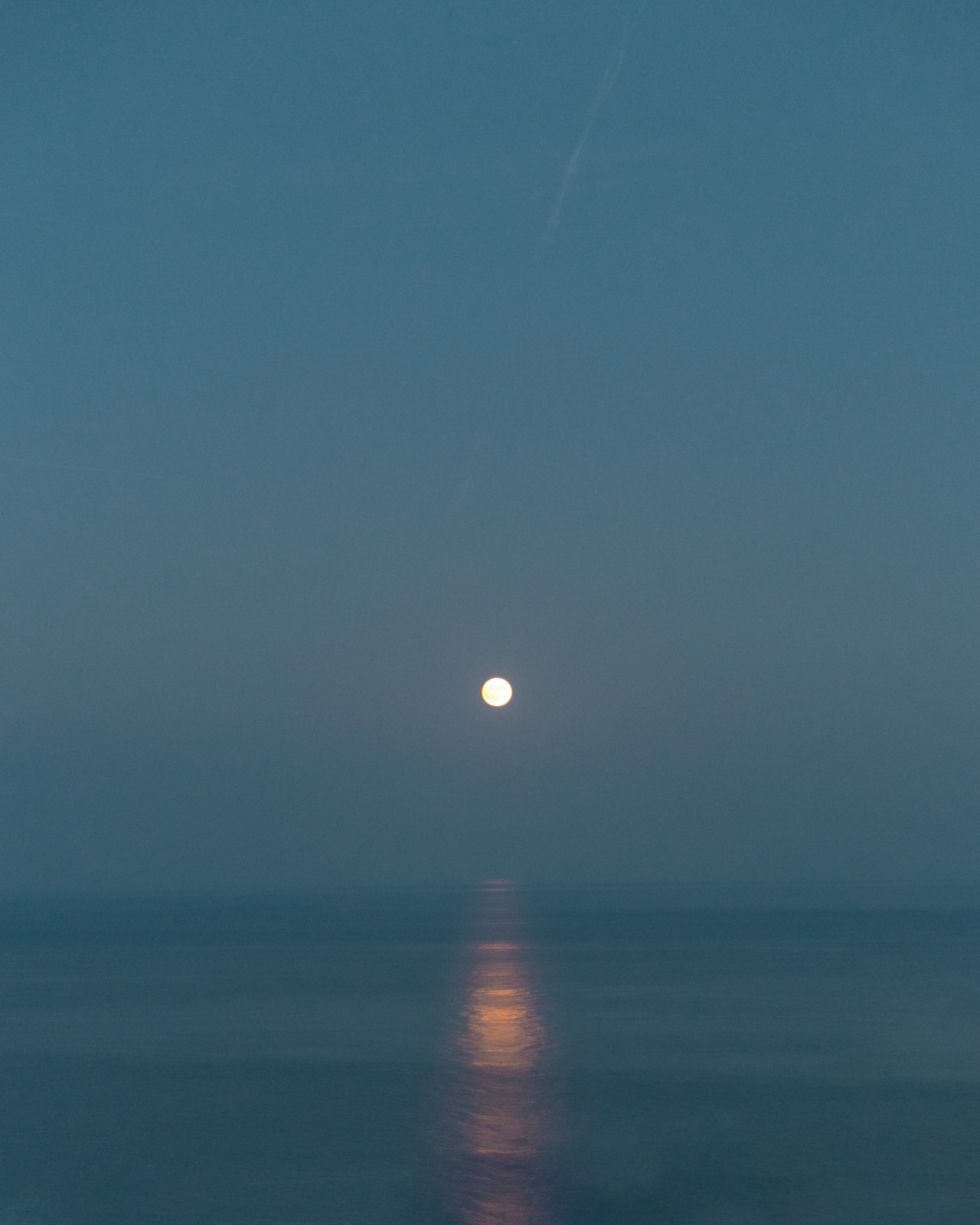 A moon sits low in the sky right above a vast sea.