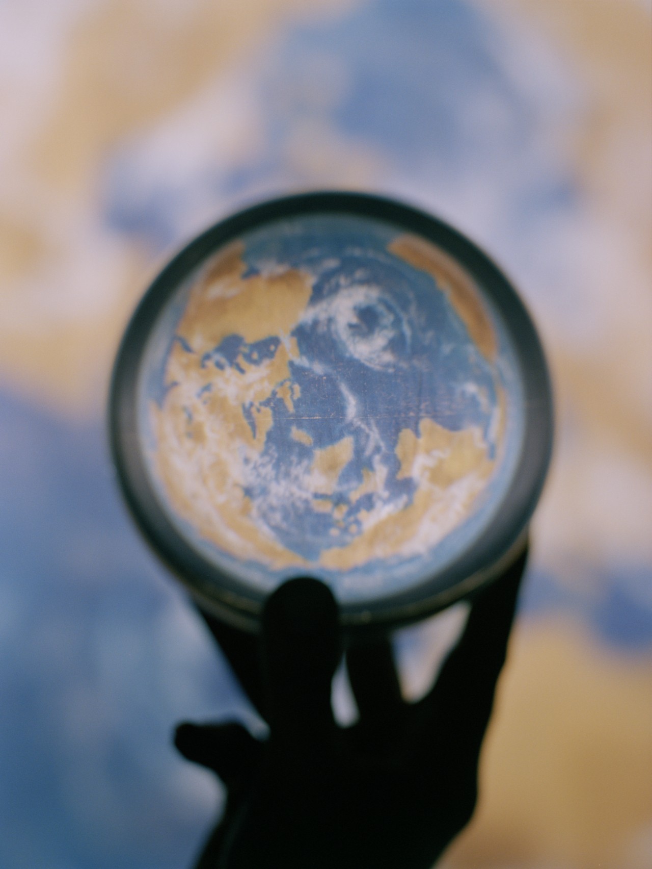 The silhouette of a hand holds a small magnifying glass depicting an aerial view of the earth.