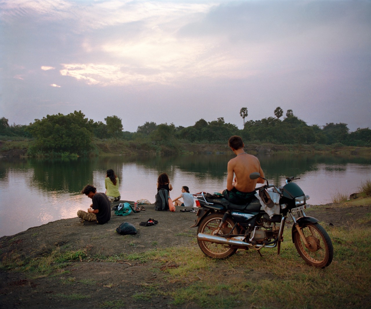 Several young people gather at the edge of a lake at sunset.