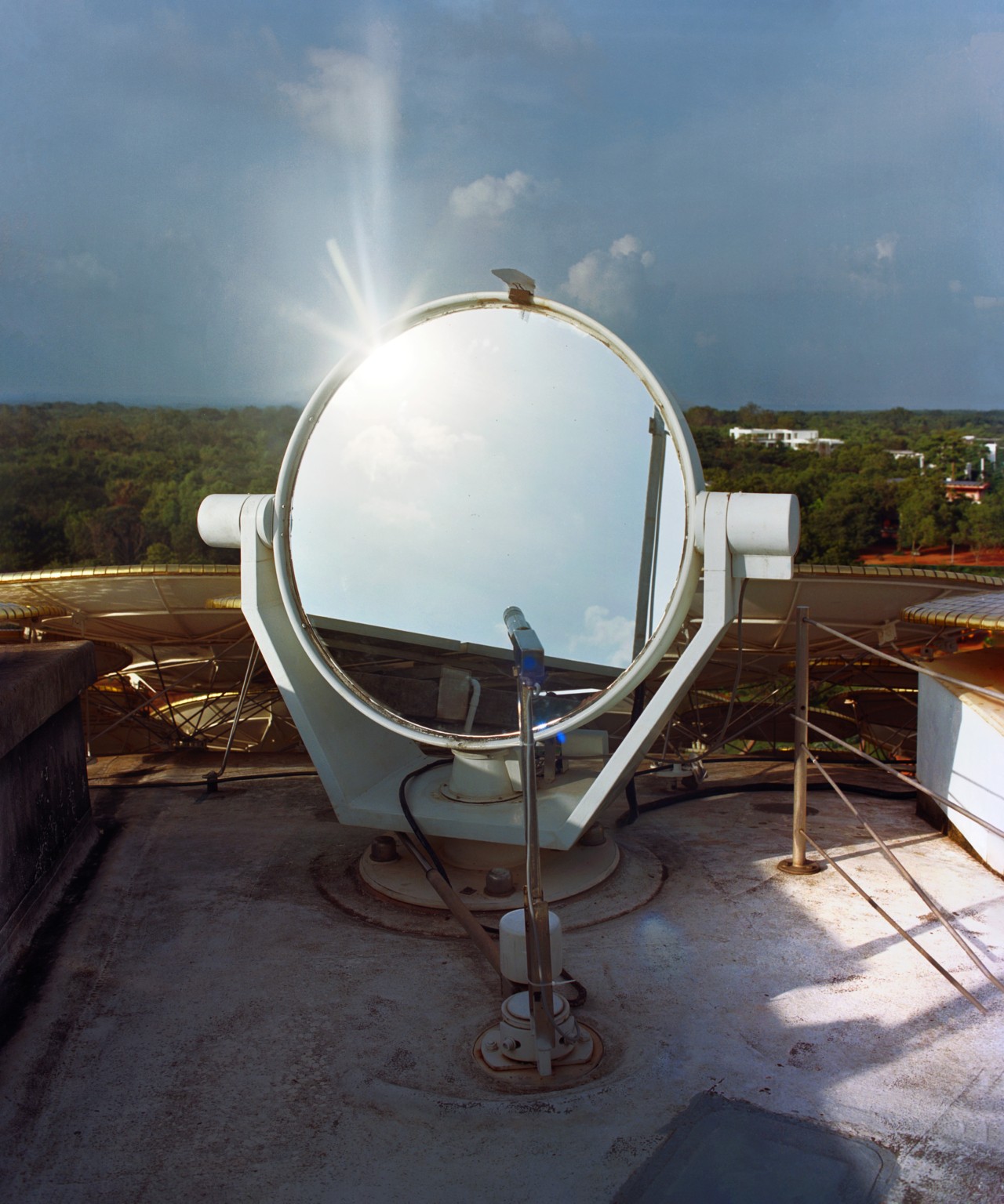 A large white mirror sits on the roof of a building, reflecting light.