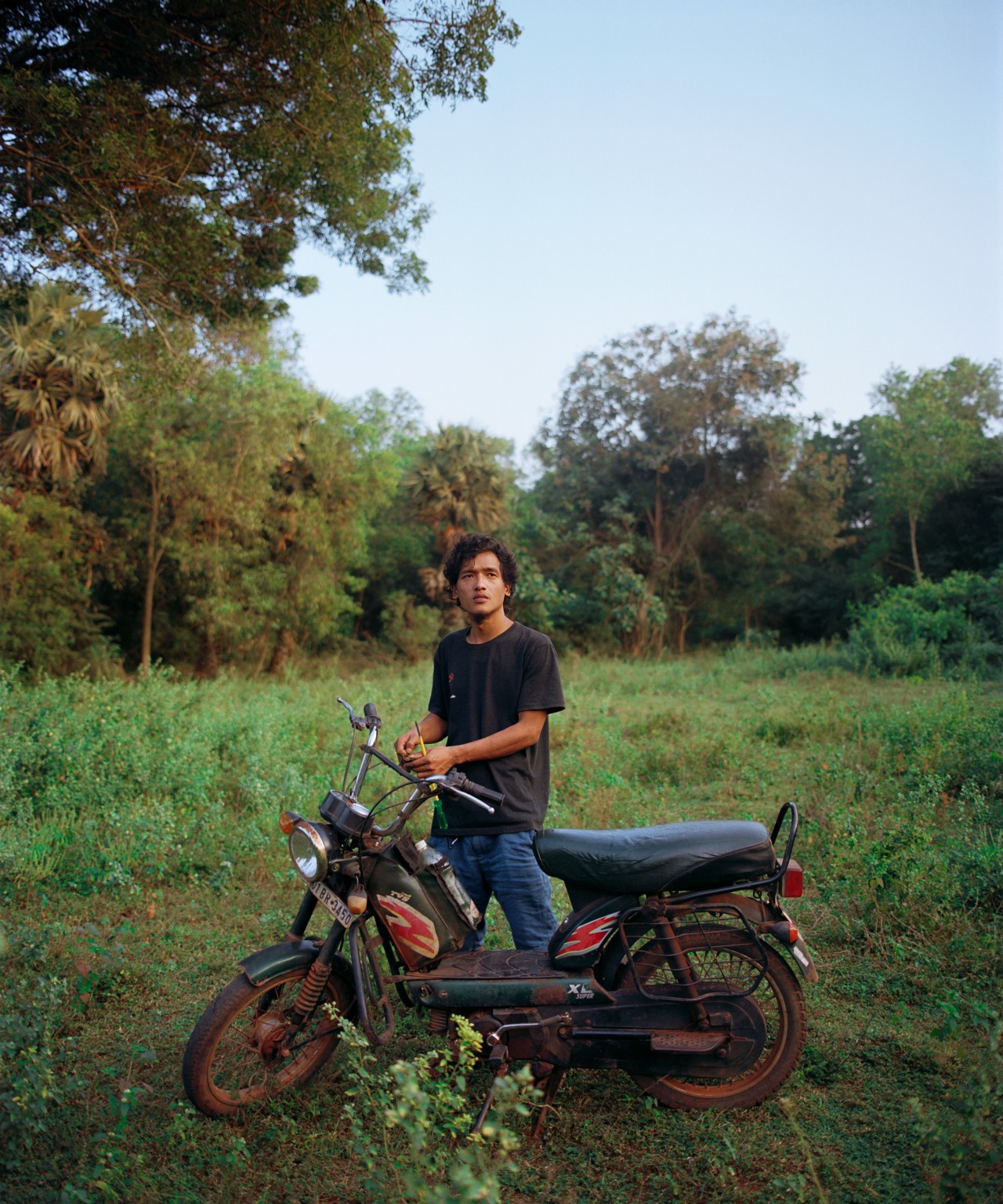 A young person posing in front of a motorcycle in a grass field.