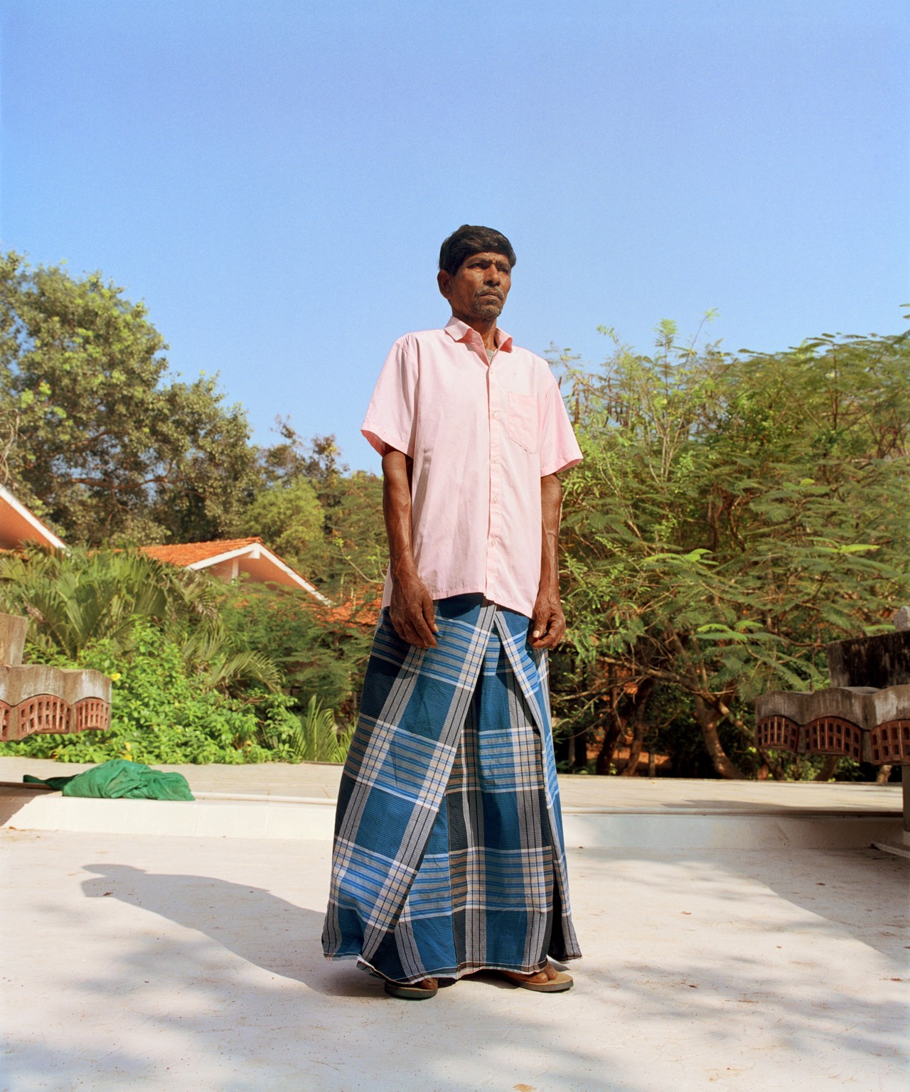 A man wearing a pink shirt poses on a cement surface.