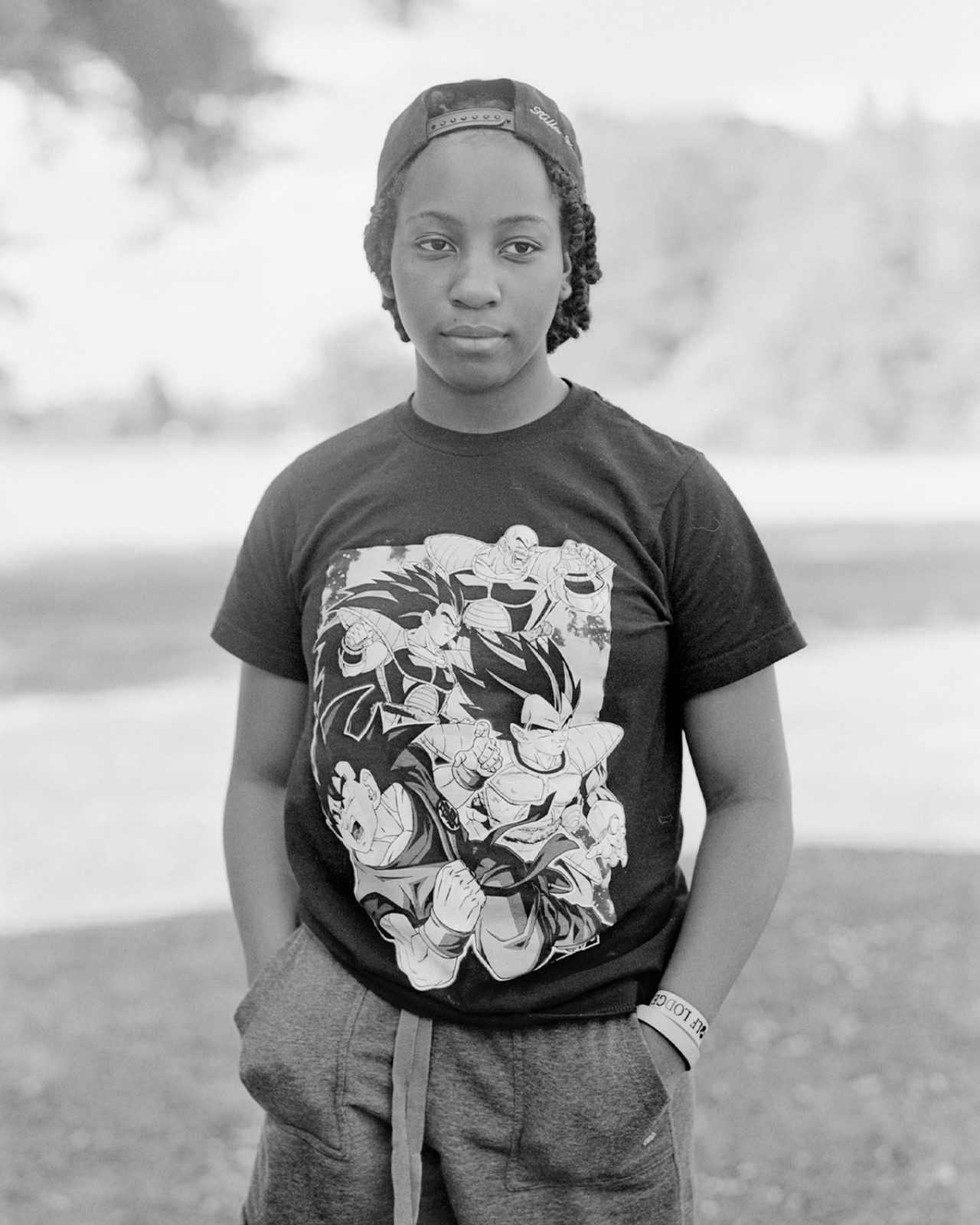 A young person wearing a hat and their hands in their pockets poses in front of a grass field.