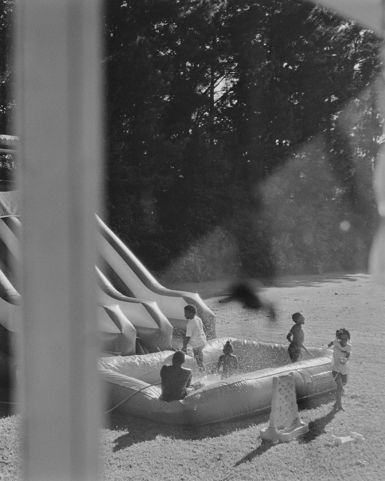 A group of children play on a water slide and inflatable pool outside of a window.