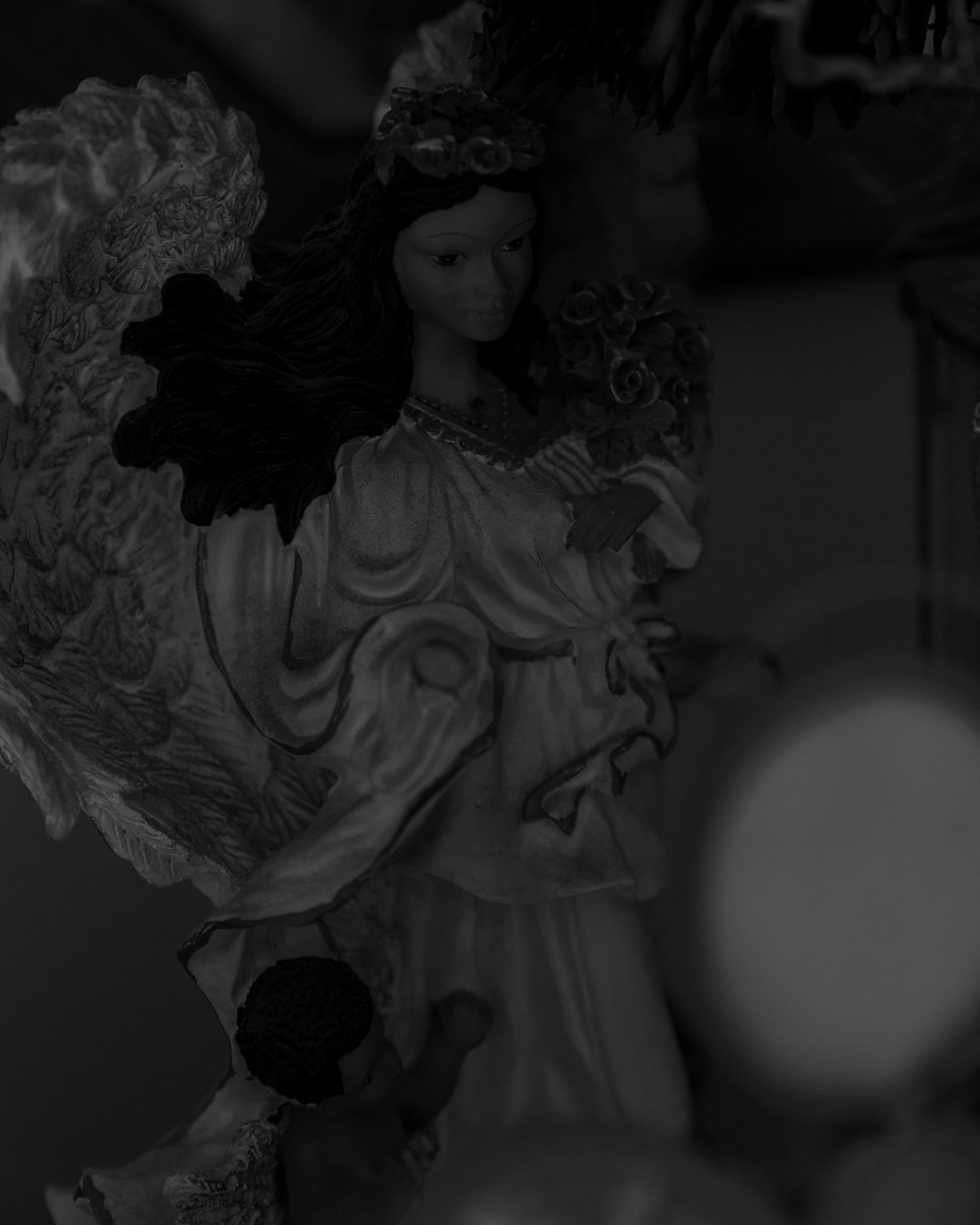 A porcelain angel doll stands still in dark lighting.