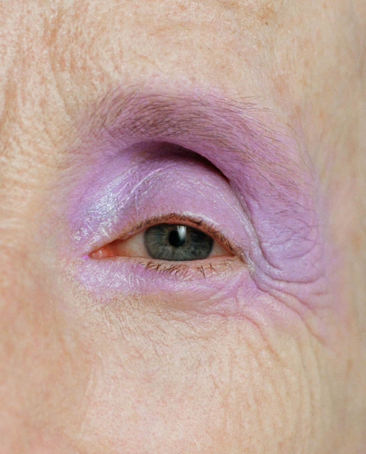 A close up of a human's blue colored eye wearing pink eyeshadow on their lid.