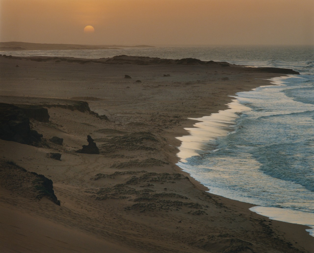 The ocean water meets the dark sand as the sun sets in La Guajira.