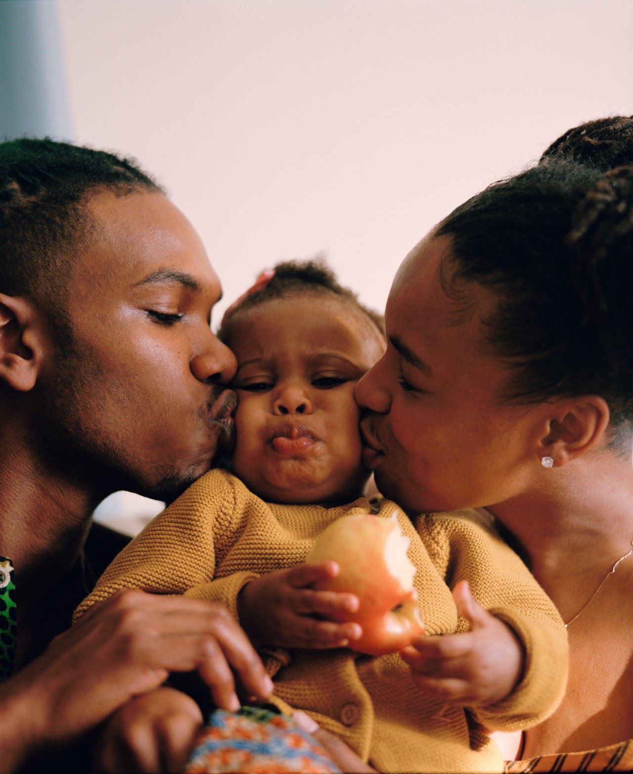 Two young parents kiss opposite cheeks of their child.