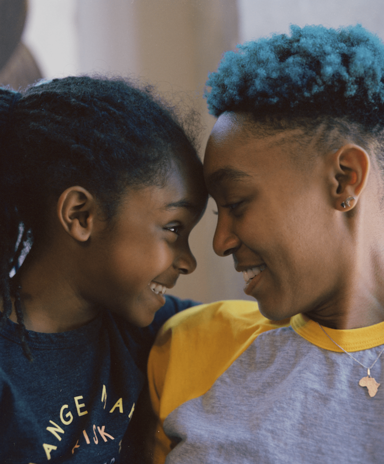A young parent and their child smile as they lean their foreheads together.